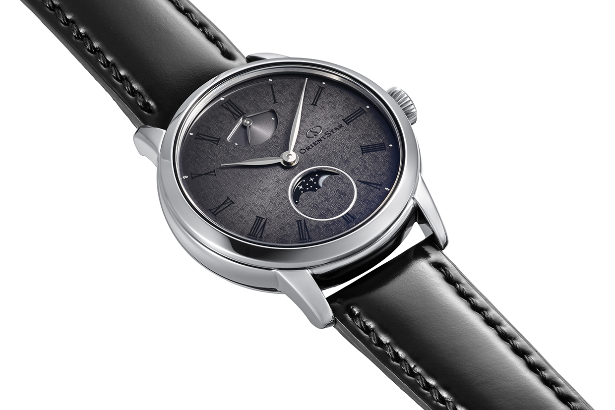Eine elegante, silberfarbene Herrenuhr mit einem dunklen, strukturierten Zifferblatt und einem Mondphasenfenster.
