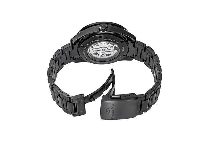 Eine schwarze, glänzende Armbanduhr mit sichtbarem Uhrwerk im geschlossenen Zustand, aber geöffnetem Verschluss. 