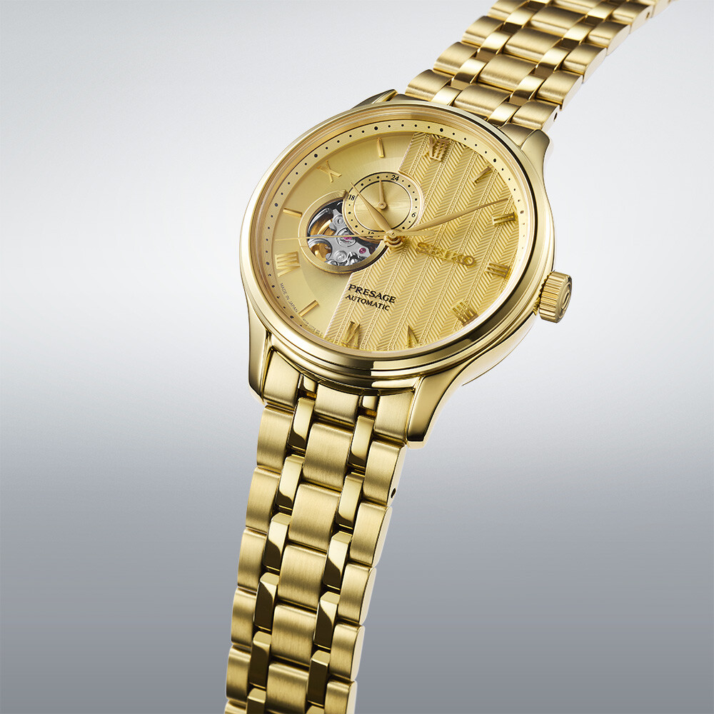 Eine goldene Armbanduhr mit einem runden Zifferblatt mit einem offenen Herz-Mechanismus und einem Chevron-Muster.