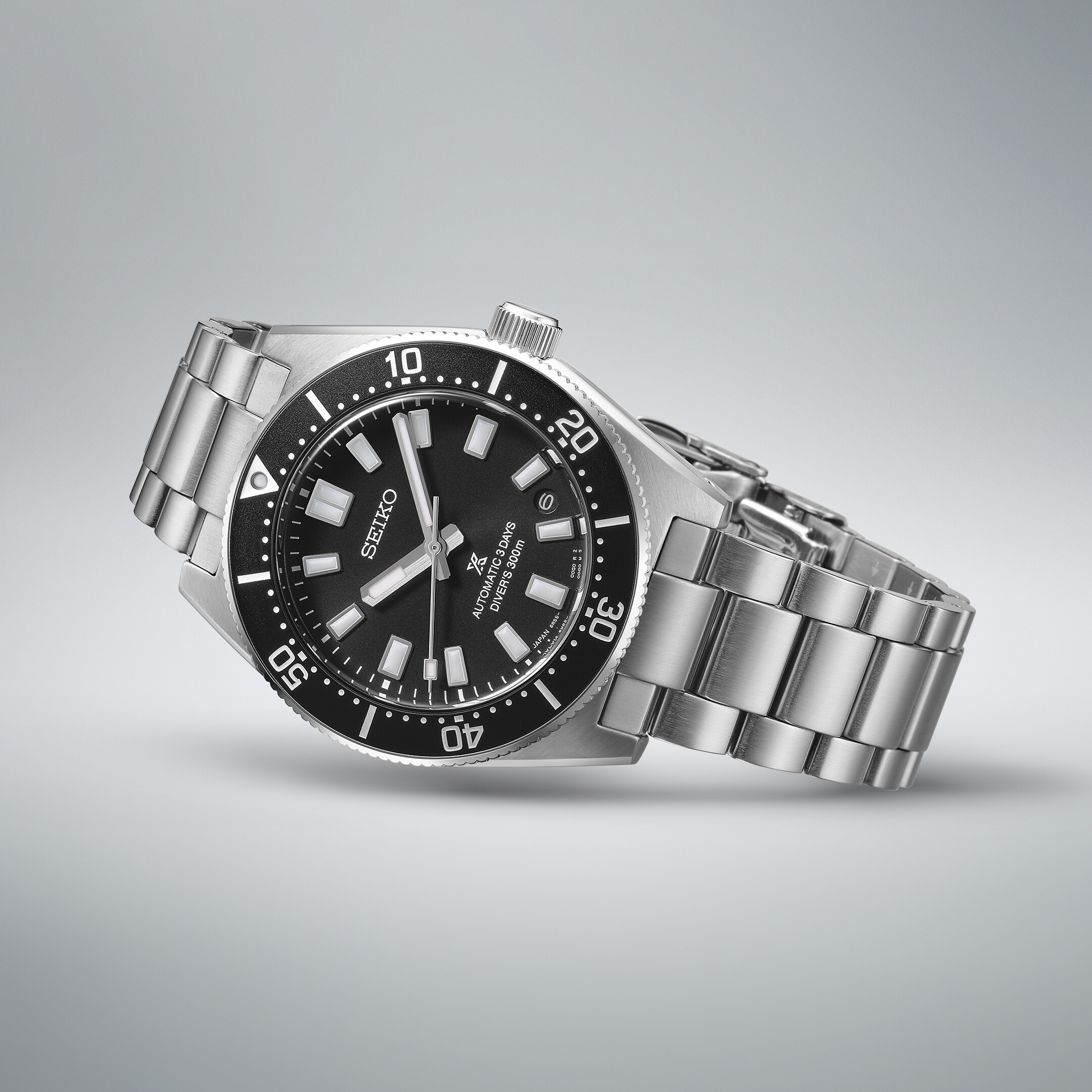Moderne silberne Herrenuhr mit schwarzem Zifferblatt und leuchtenden Zeigern, auf grauem Hintergrund.