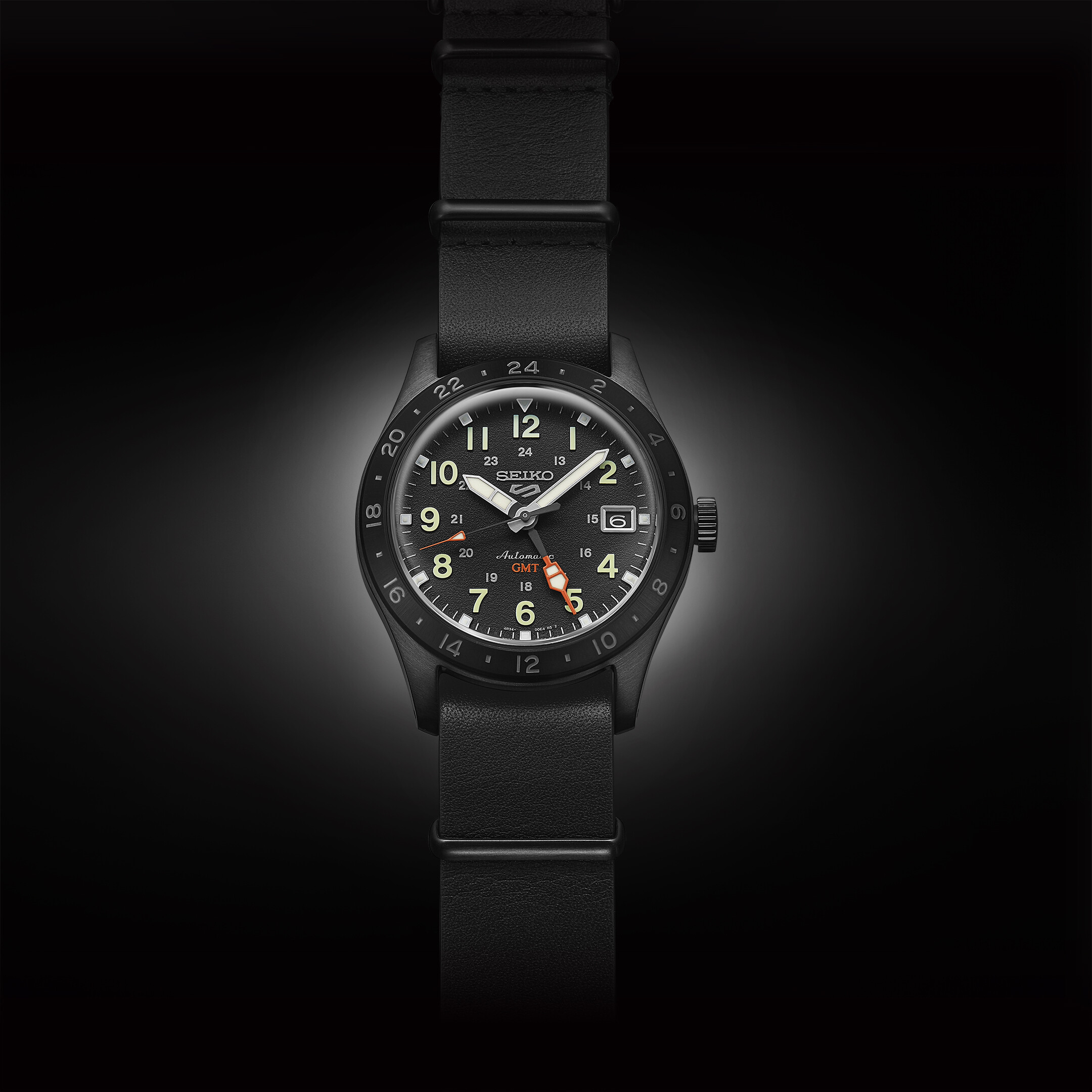 Schwarze Herrenuhr mit schwarzem Lederarmband und Zifferblatt mit Leuchtzeigern und orangefarbenem GMT-Zeiger.