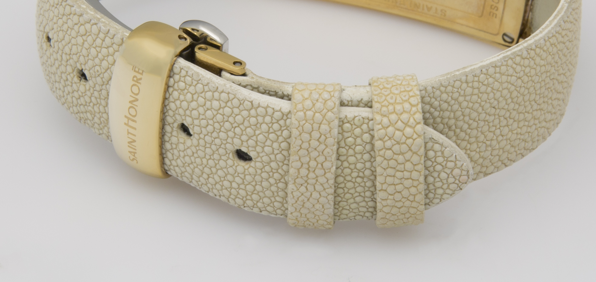 Ein hellbeiges Armbandmuster mit einer goldenen Schnalle. Das Muster ist regelmäßig und besteht aus kleinen Kreisen.
