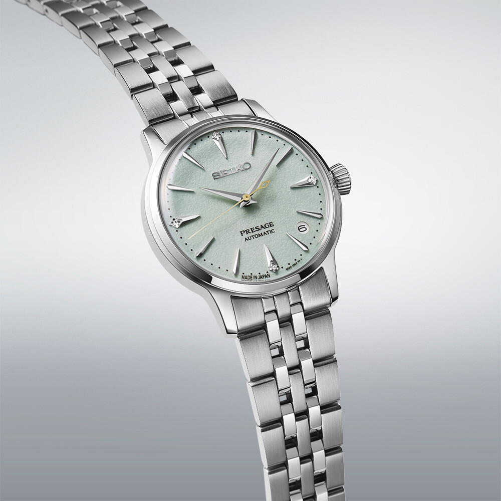 Ein silbernes Damenarmbanduhr mit einem hellgrünen Zifferblatt, das mit kleinen Diamanten als Stundenmarkierungen verziert ist.