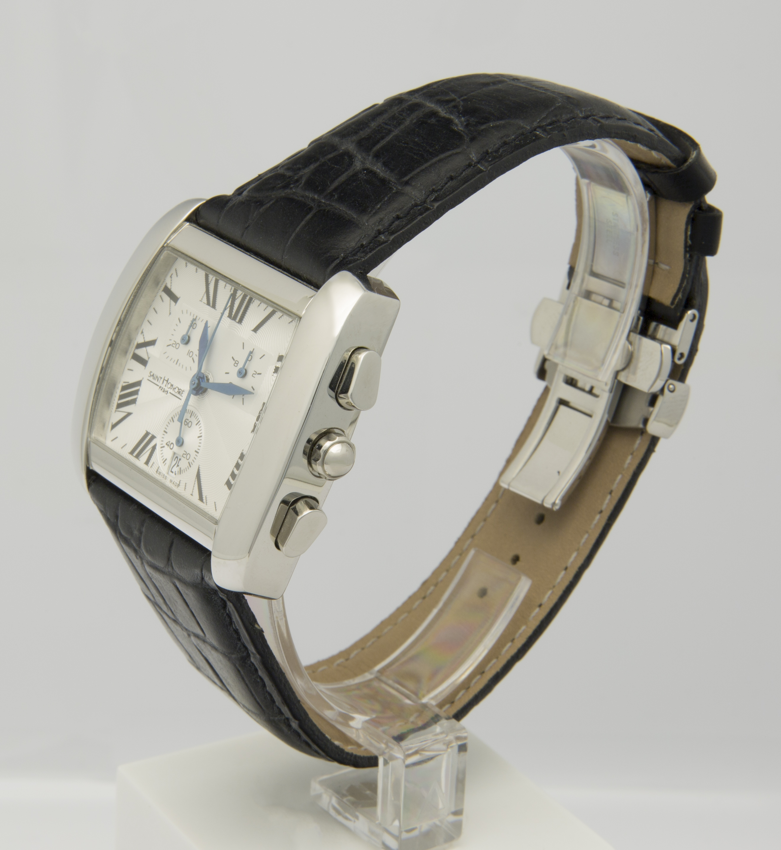 Eine rechteckige Armbanduhr mit weißem Zifferblatt, schwarzen römischen Ziffern und blauem Zeigern auf einem schwarzen Krokodillederarmband.