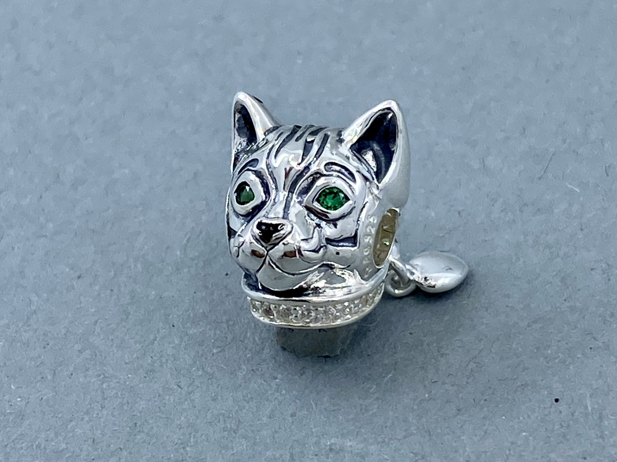 Ein silbernes Anhänger in Form eines Katzenkopfes mit grünen Augen und gestreiften Mustern.