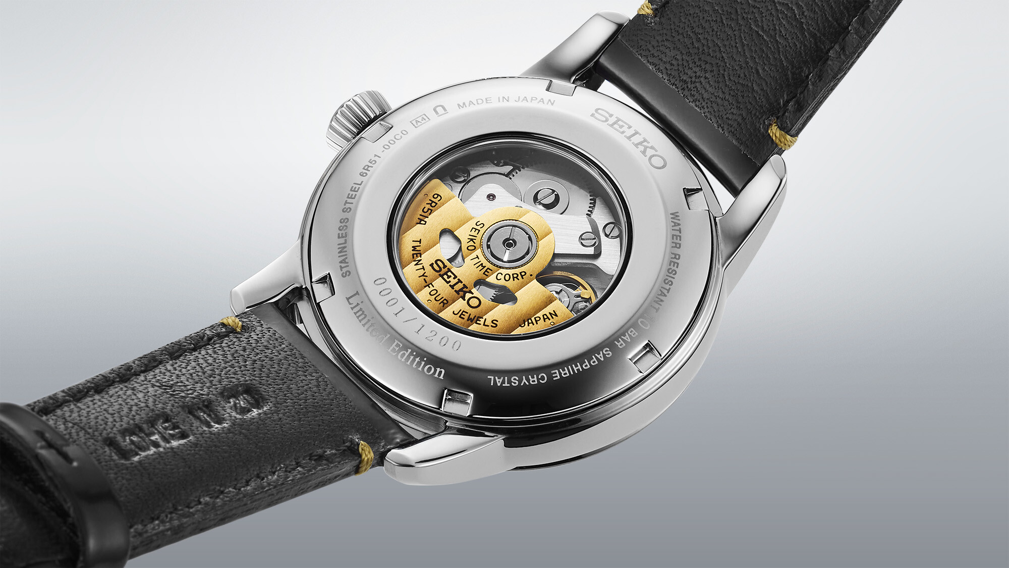 Eine automatische Uhr mit schwarzem Lederarmband und einem durchsichtigen Gehäuseboden, der das goldene Uhrwerk freigibt.