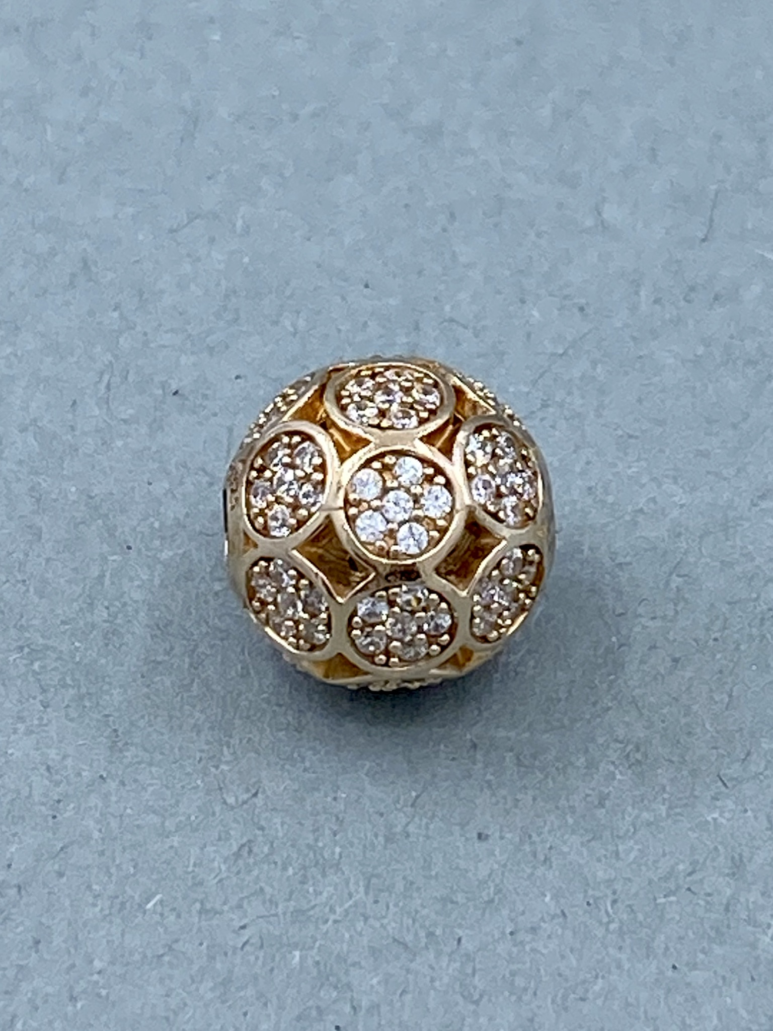Eine goldene Kugel mit einem durchbrochenen Muster, besetzt mit vielen kleinen, funkelnden Steinen.