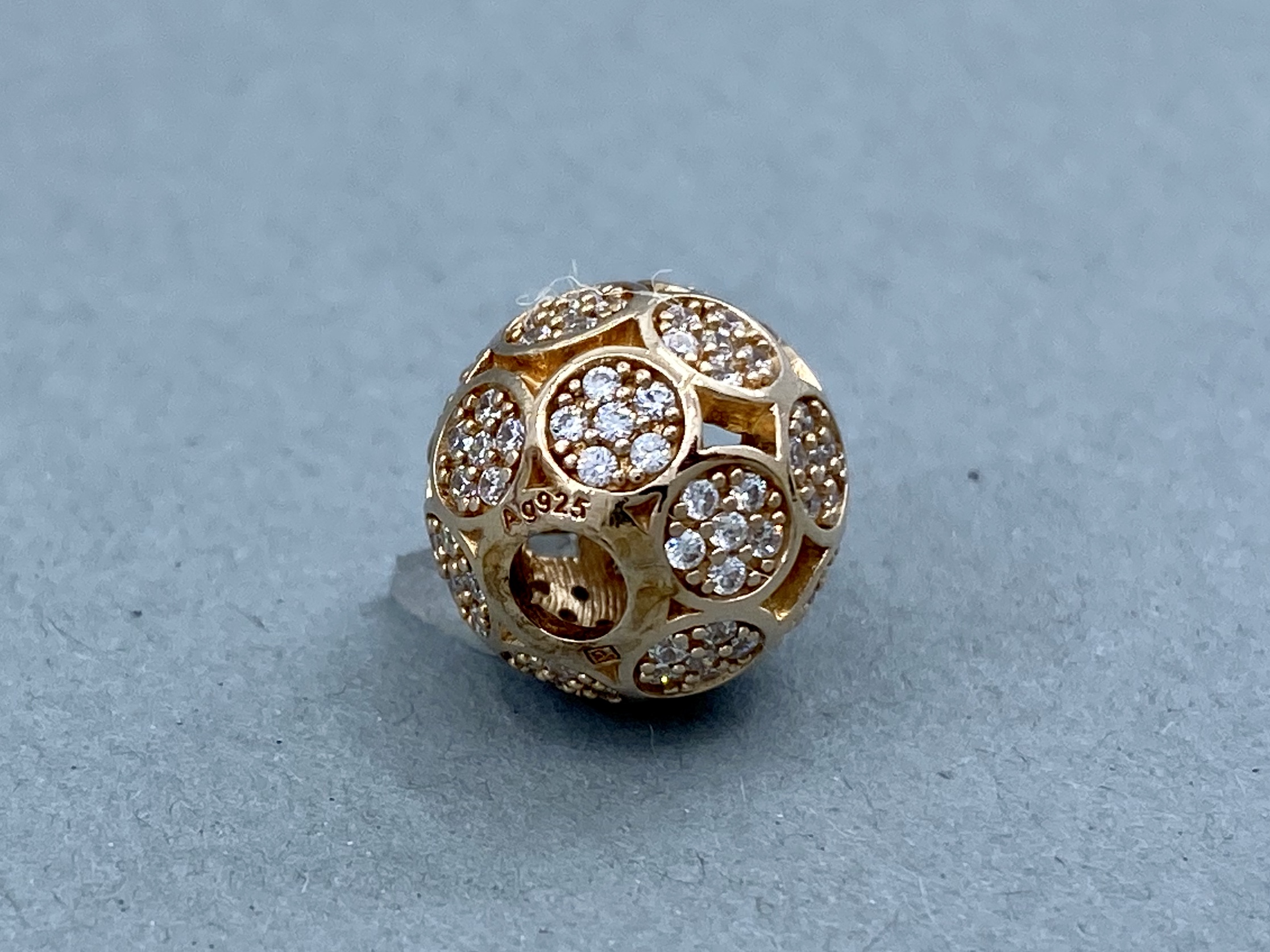 Ein kugelförmiges Schmuckteil in Gold mit vielen runden Vertiefungen, die mit kleinen, glitzernden Steinen besetzt sind.