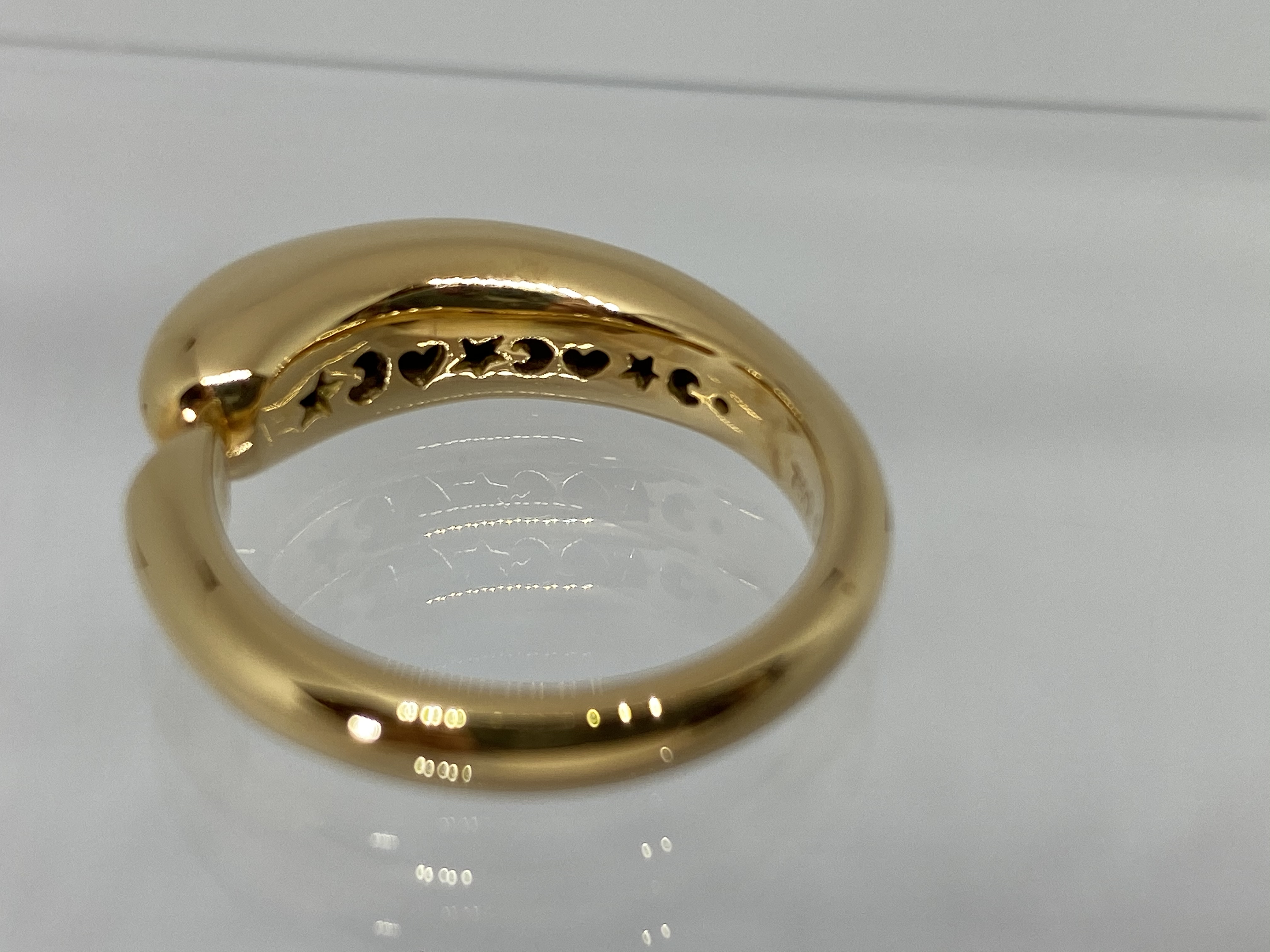 Ein goldener Ring mit einer gewölbten Form und eingravierten Herzen und Sternen auf der Innenseite.
