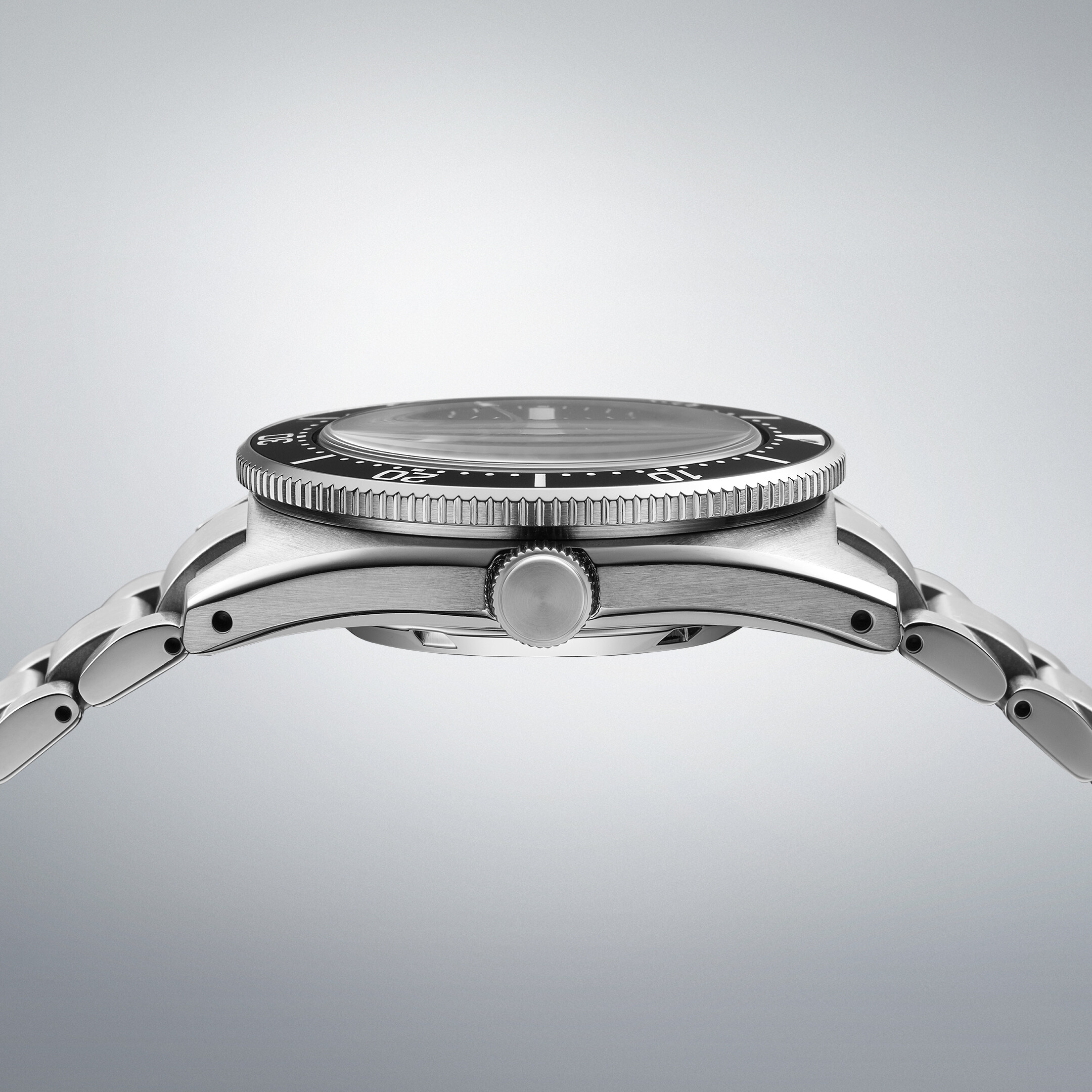 Eine Armbanduhr mit schwarzem Zifferblatt und Drehlünette, seitlich aufgenommen mit einem Armband aus Metall.