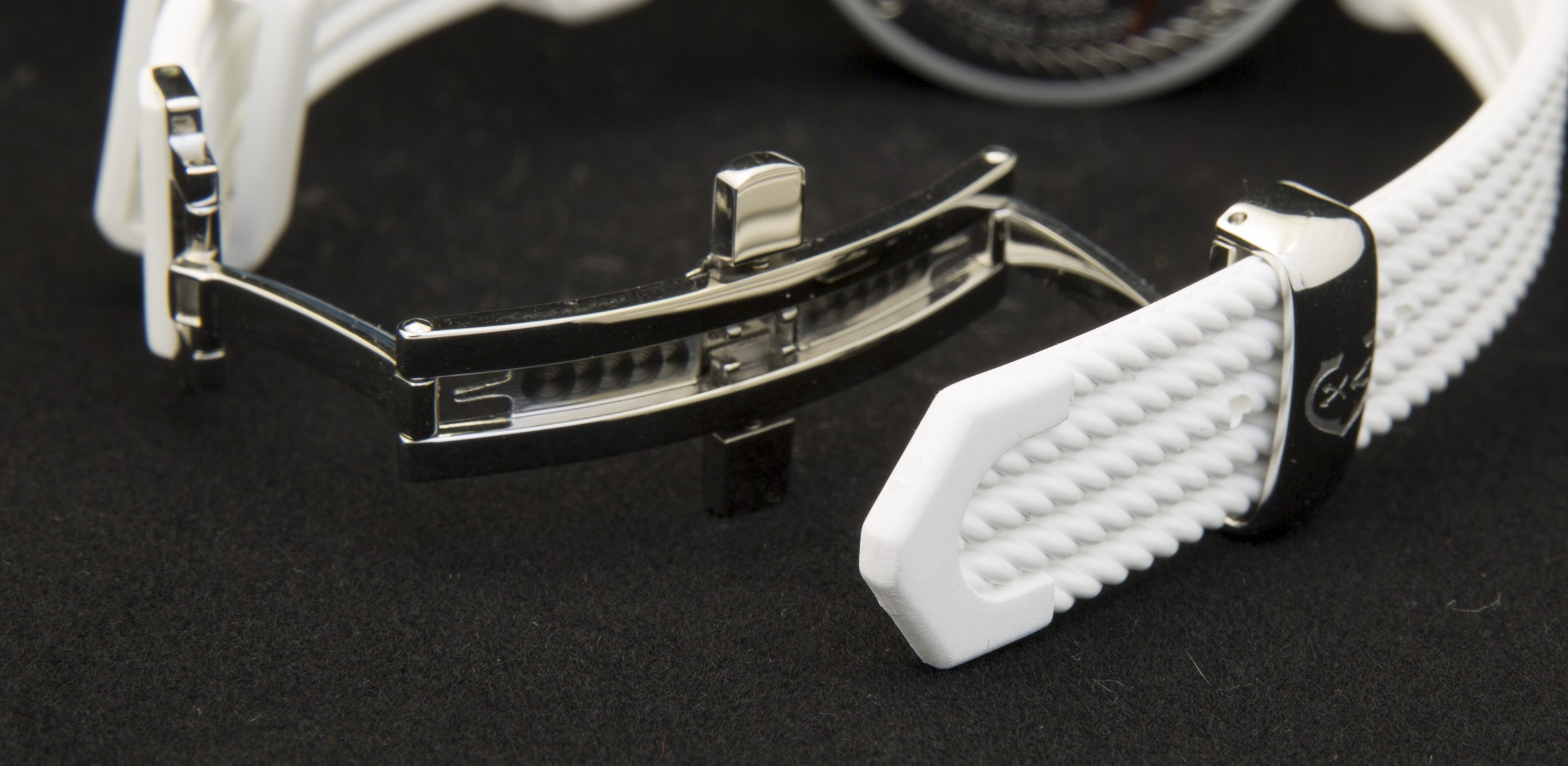 Ein weißes Armband mit einem Rillenmuster und einer silbernen Schnalle liegt auf einem schwarzen Hintergrund.