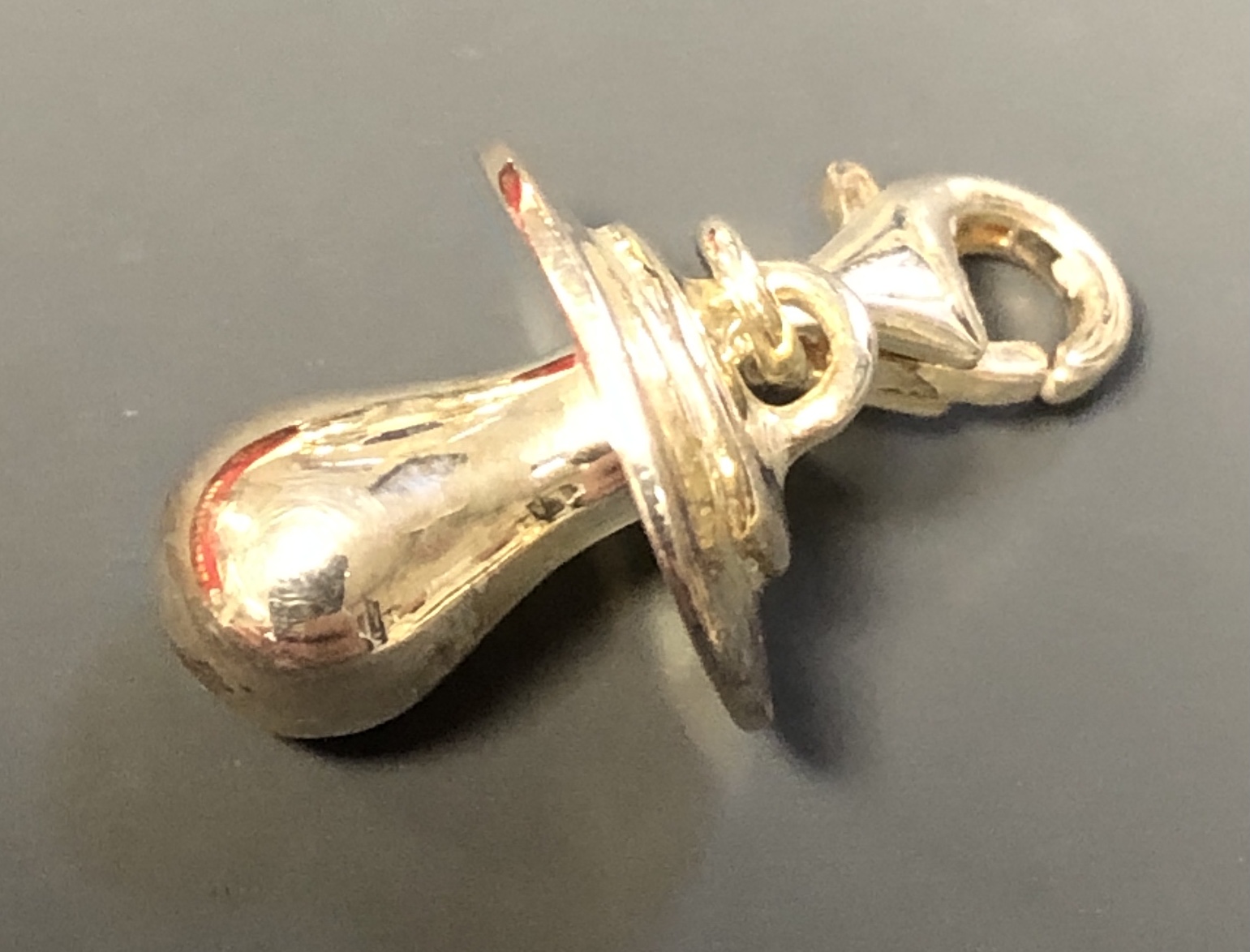 Ein glänzender Thomas Sabo Schnuller-Anhänger in Gold mit einem Karabinerverschluss ist auf einem dunklen Hintergrund zu sehen.