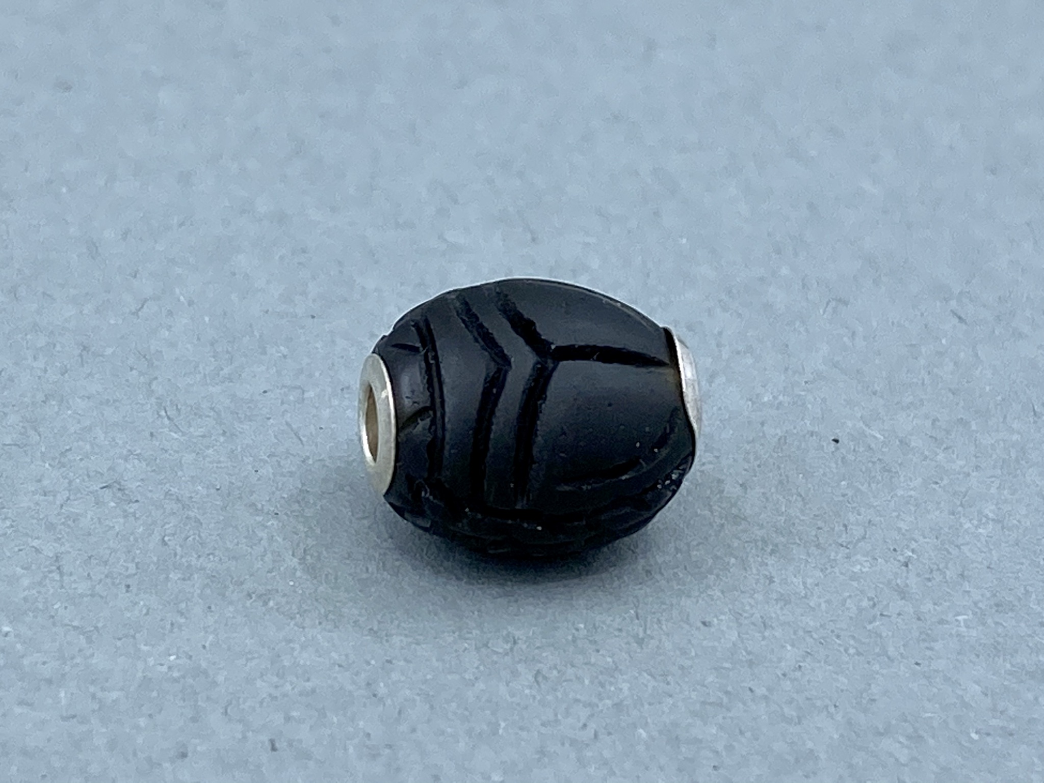 Ein schwarzer ovaler Anhänger mit eingekerbtem Muster und silbernen Endkappen.