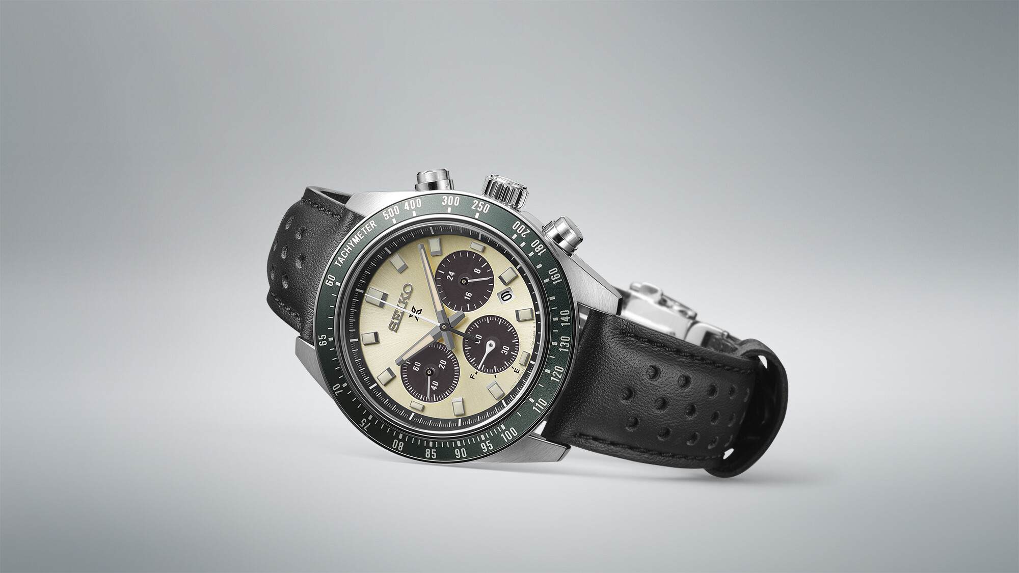 Eine Herrenuhr mit cremefarbenem Zifferblatt, schwarzen Hilfszifferblättern und einem schwarzen Lederarmband mit Lünette mit grüner Skala.