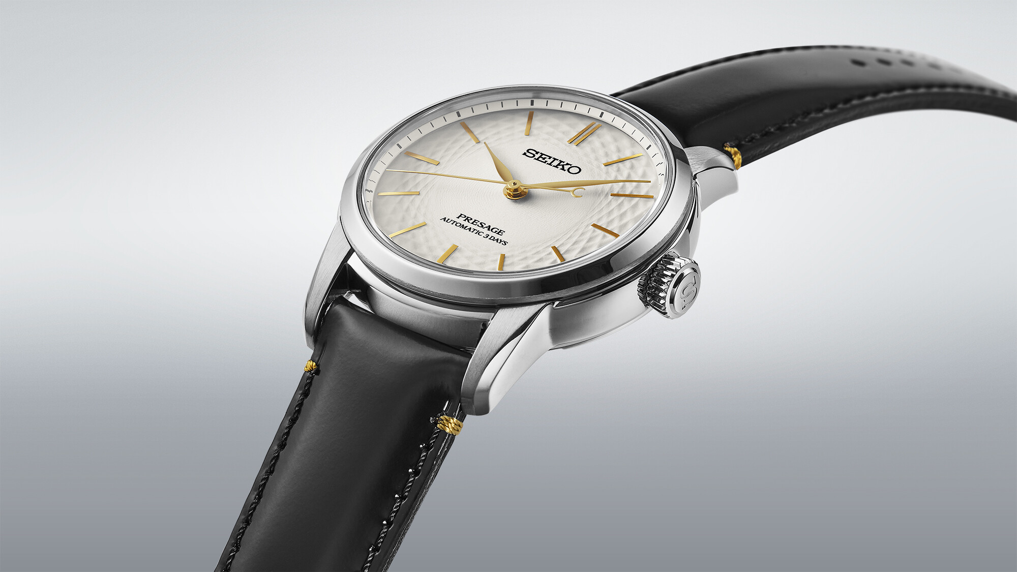 Eine silberne Uhr mit weißem Zifferblatt und goldenen Zeigern, getragen an einem schwarzen Armband.
