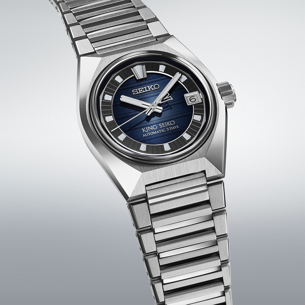 Eine silberne Armbanduhr mit blauem Zifferblatt und horizontalen Linien. Das Datum ist sichtbar.