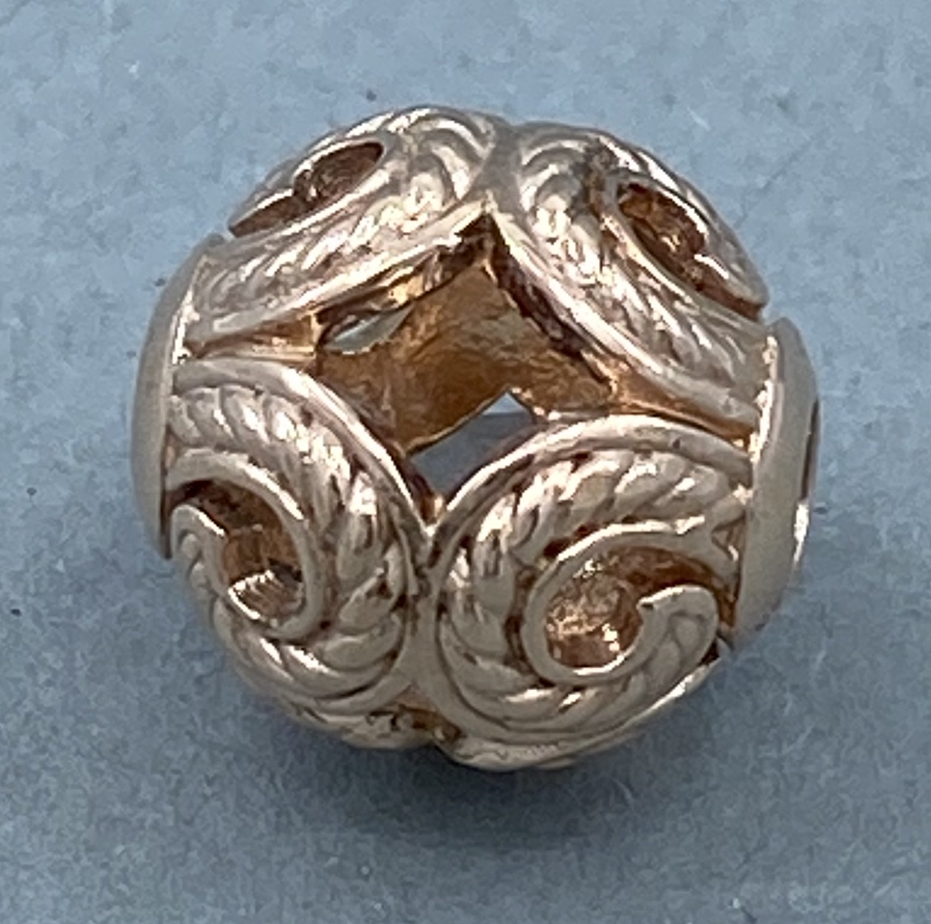 Eine goldene Kugel mit filigranen Blattmustern, die wie ein offenes Geflecht gestaltet ist.