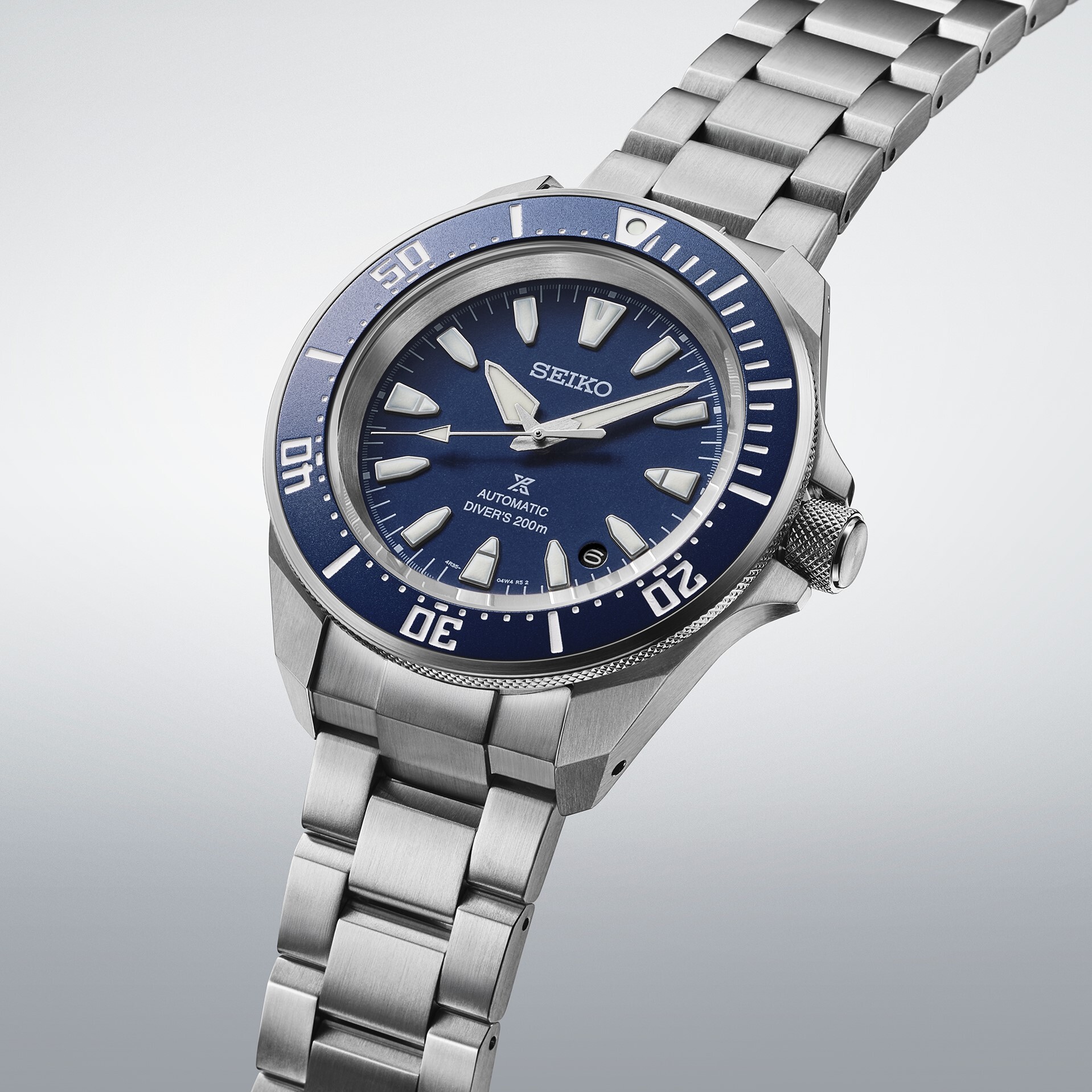Eine silberfarbene Taucheruhr mit blauem Zifferblatt und silbernem Armband, die auf einer hellgrauen Fläche schwebt.
