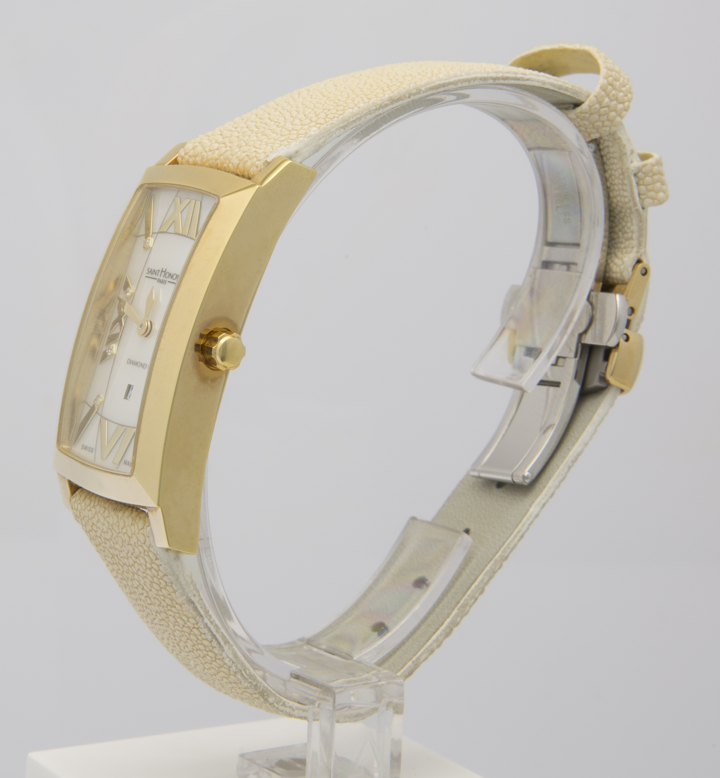 Ein rechteckiges goldfarbenes Damenarmbanduhr mit römischen Ziffern und einem hellbeigen Armband mit Muster.