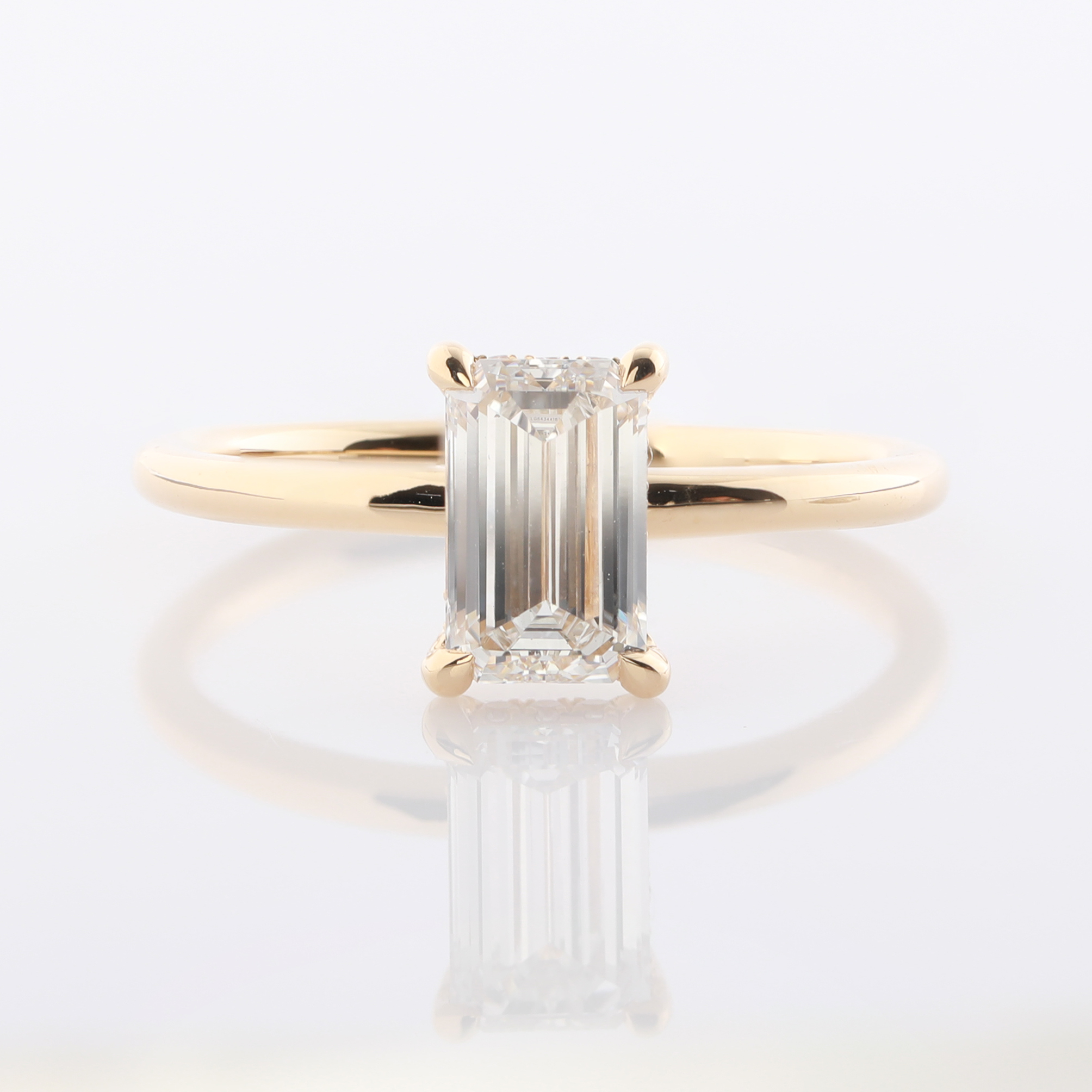 Ein goldener Ring mit einem rechteckigen, geschliffenen Stein, der an den Ecken gehalten wird.