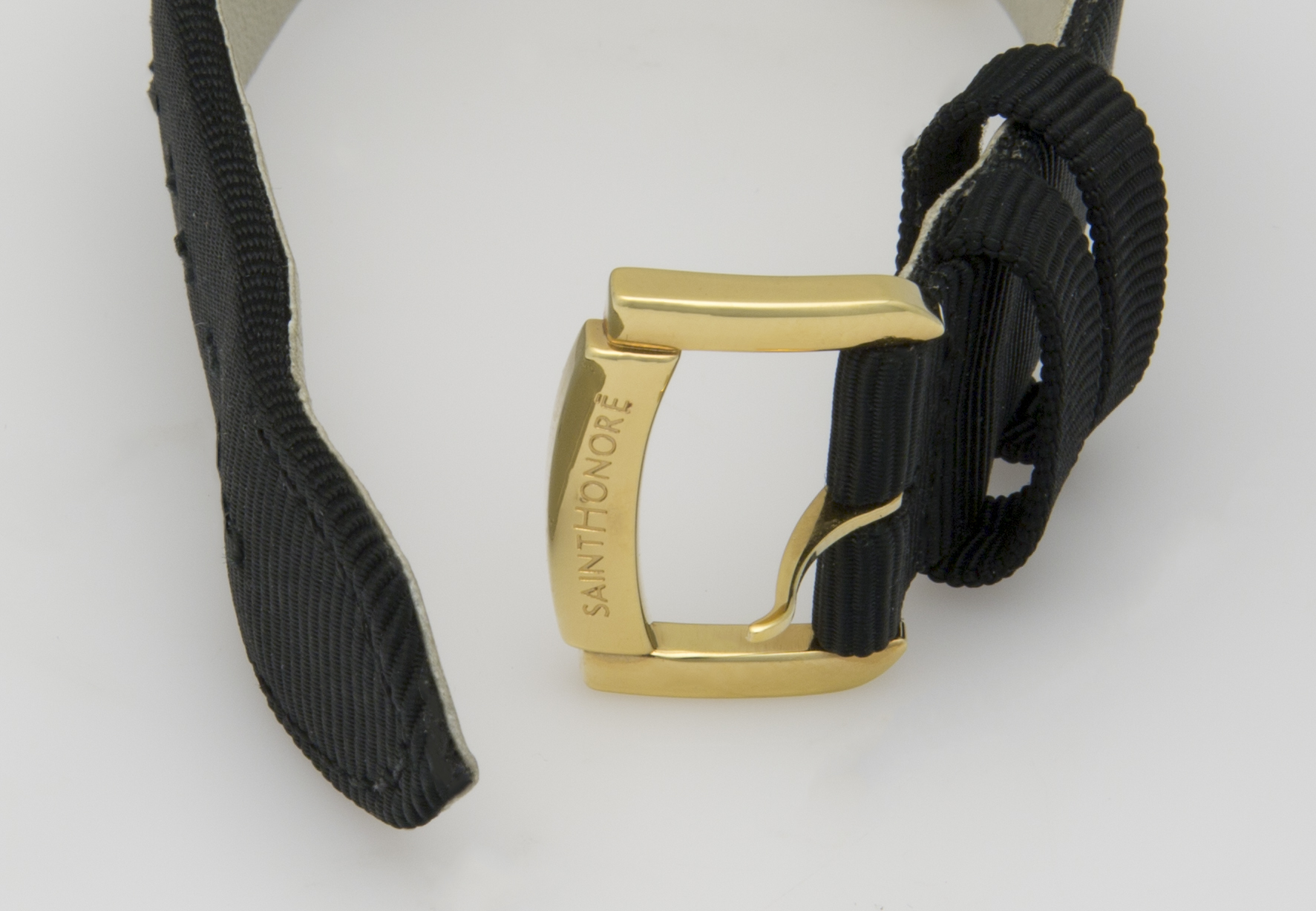Ein goldfarbenes Schnallenband mit schwarzem Gewebe wird gezeigt. Auf dem Band ist SAINT-HONORÉ eingraviert.