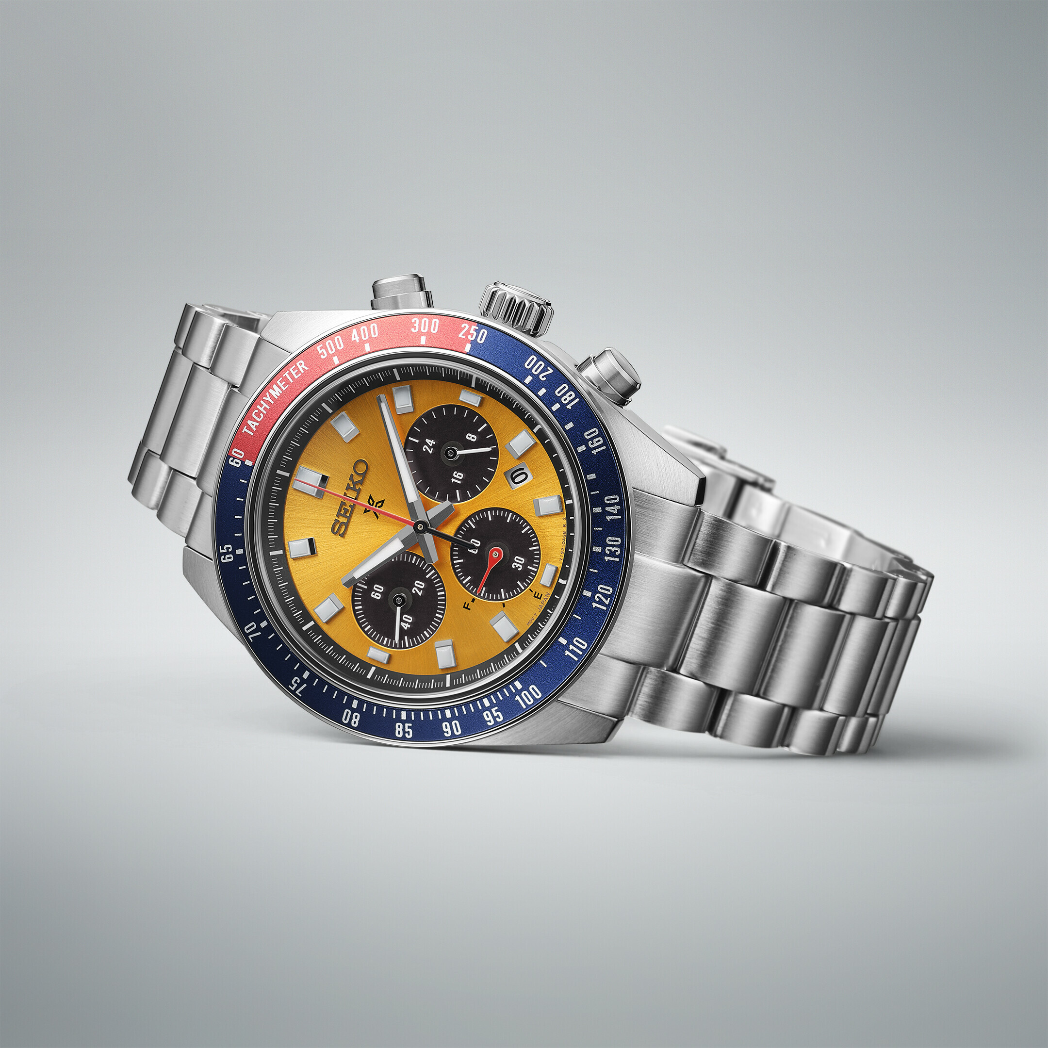 Ein silbernes Chronographen-Armbanduhr mit einem gelben Zifferblatt, roten und blauen Akzenten und drei schwarzen Hilfszifferblättern.