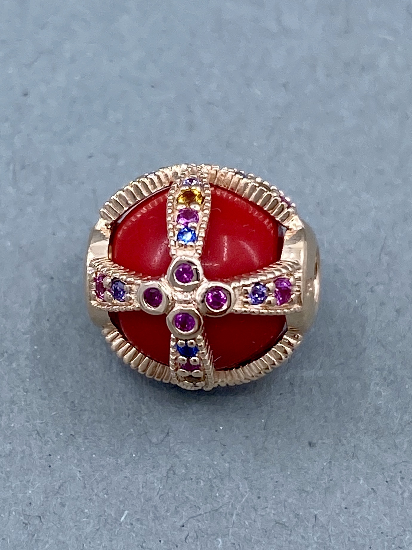 Eine rote Kugel mit einem goldenen Kreuz, verziert mit bunten Edelsteinen, als Charm.