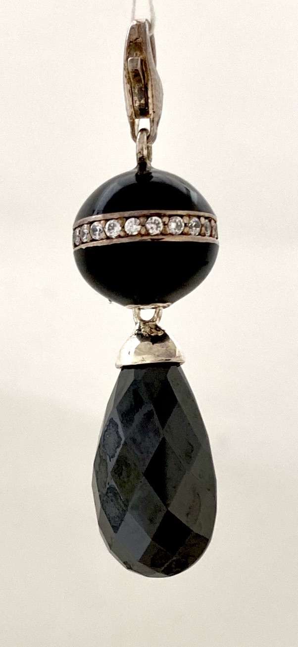 Ein schwarzer runder Stein ist von kleinen weißen Steinen umringt, darunter hängt ein tropfenförmiger schwarzer Stein.