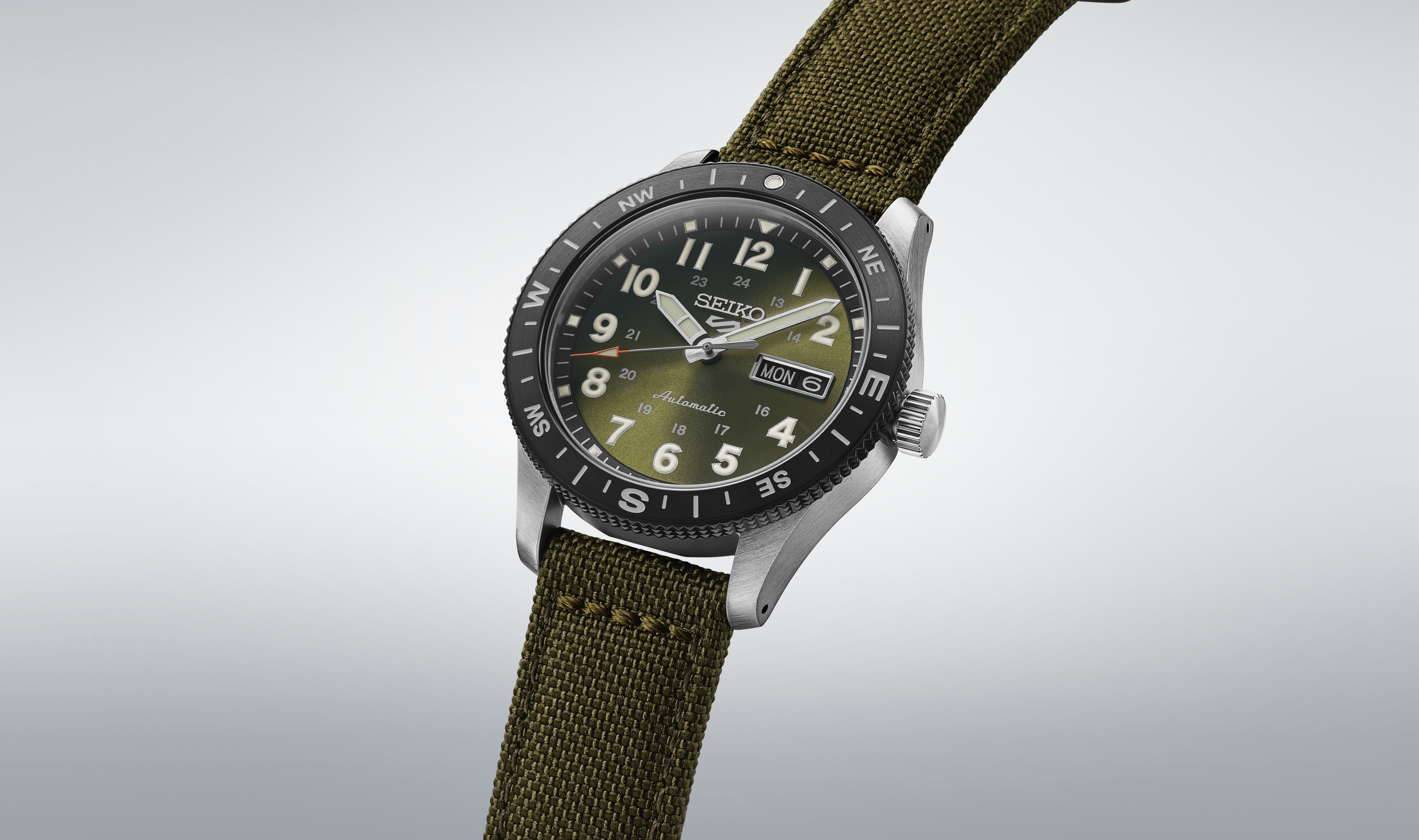 Armbanduhr mit einem grünen Zifferblatt und einem dunklen Rand, kombiniert mit einem olivgrünen Stoffarmband.