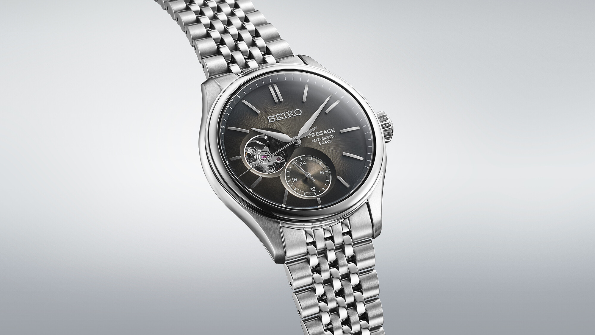 Eine silberne Armbanduhr mit grauem Zifferblatt und offenliegendem Uhrwerk.