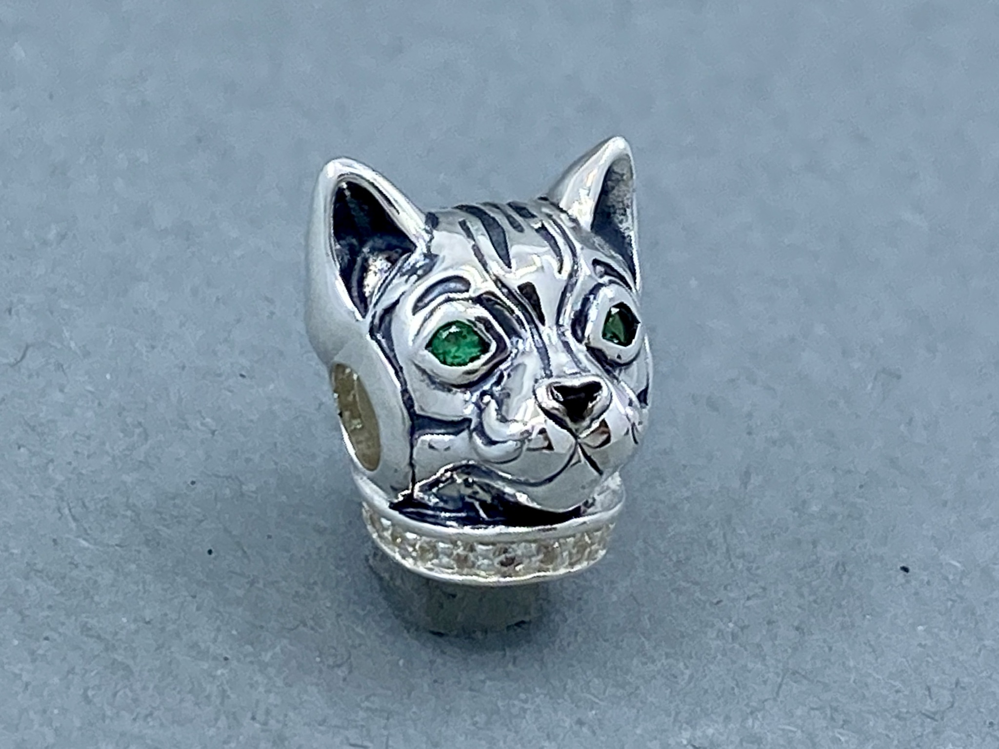 Ein silbernes Katzenkopf-Charm mit grünen Augen und dunklen Streifen