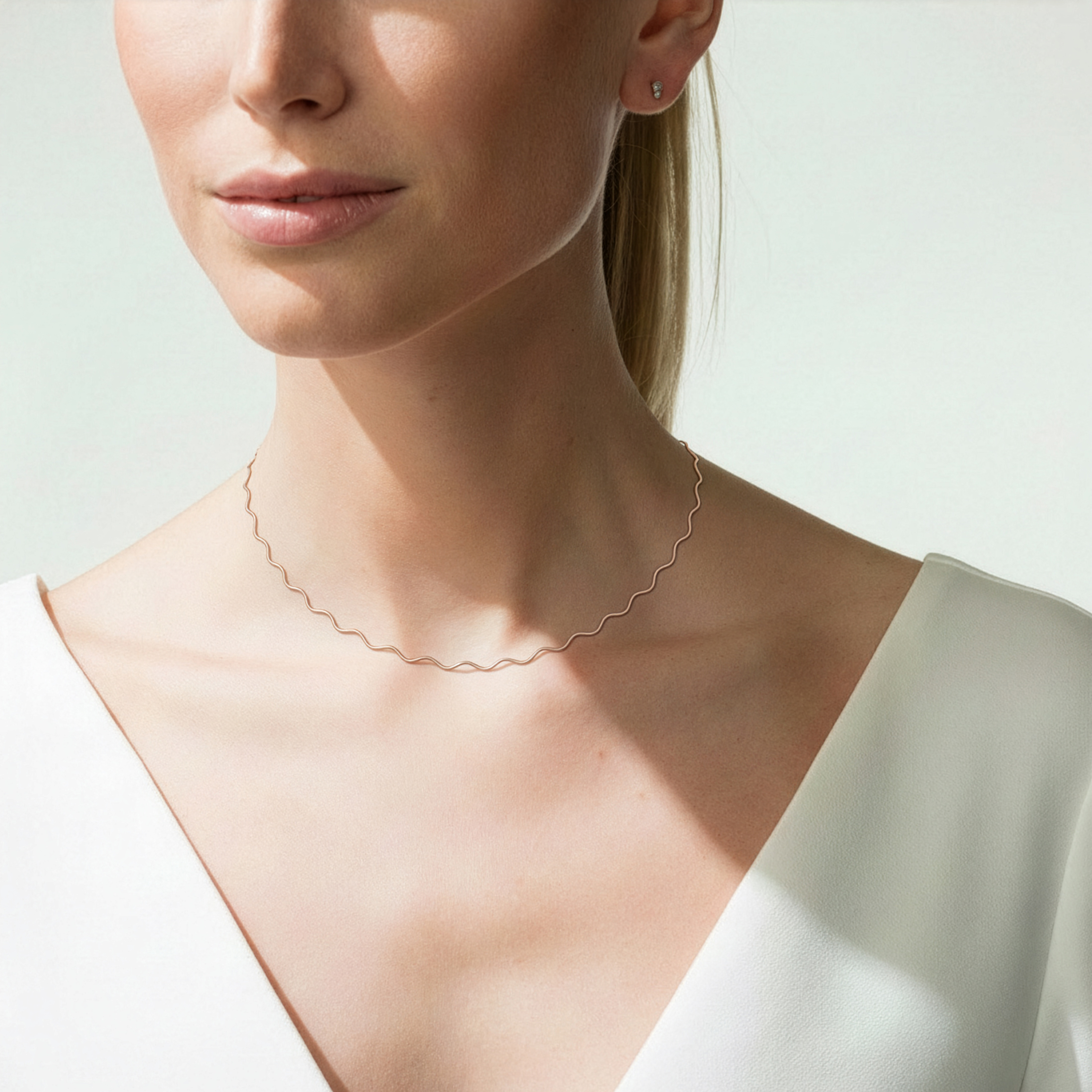 Eine Frau trägt eine zierliche Halskette mit wellenförmigem Design aus Roségold.