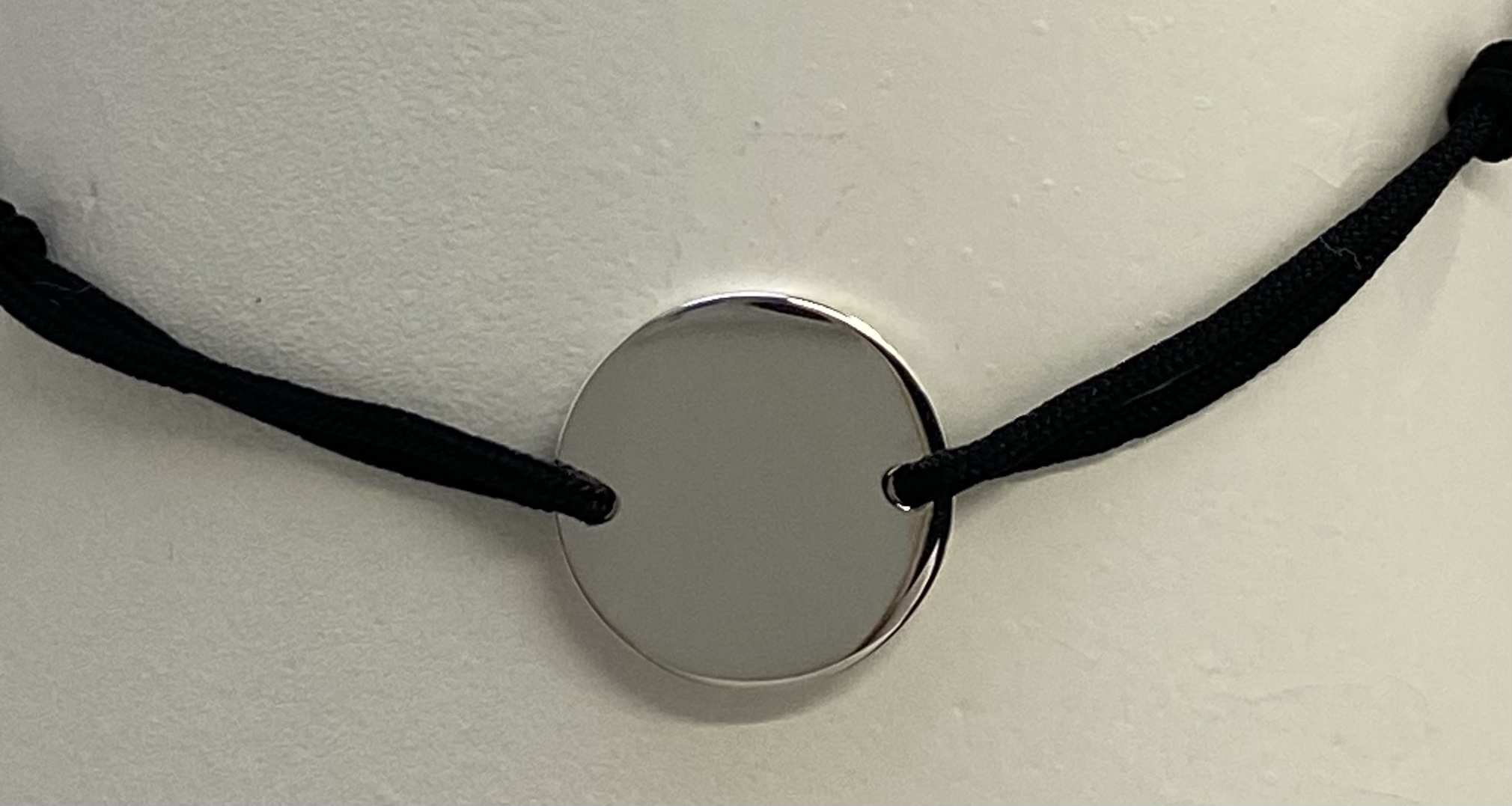 Ein glänzendes, rundes Anhänger mit schwarzem Band. Das Anhänger ist auf einem hellen Hintergrund.