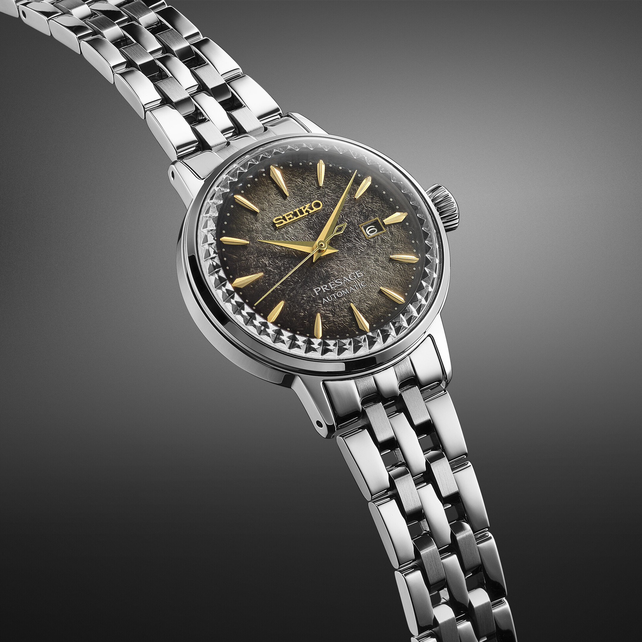 Eine silberne Armbanduhr mit einem Zifferblatt in Grau und Gold mit einem ausgeprägten Muster, gehalten in einem Vollbild.