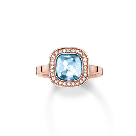 Ein roségoldener Ring mit einem großen, hellblauen, quadratischen Stein, umgeben von kleinen, klaren Steinen.