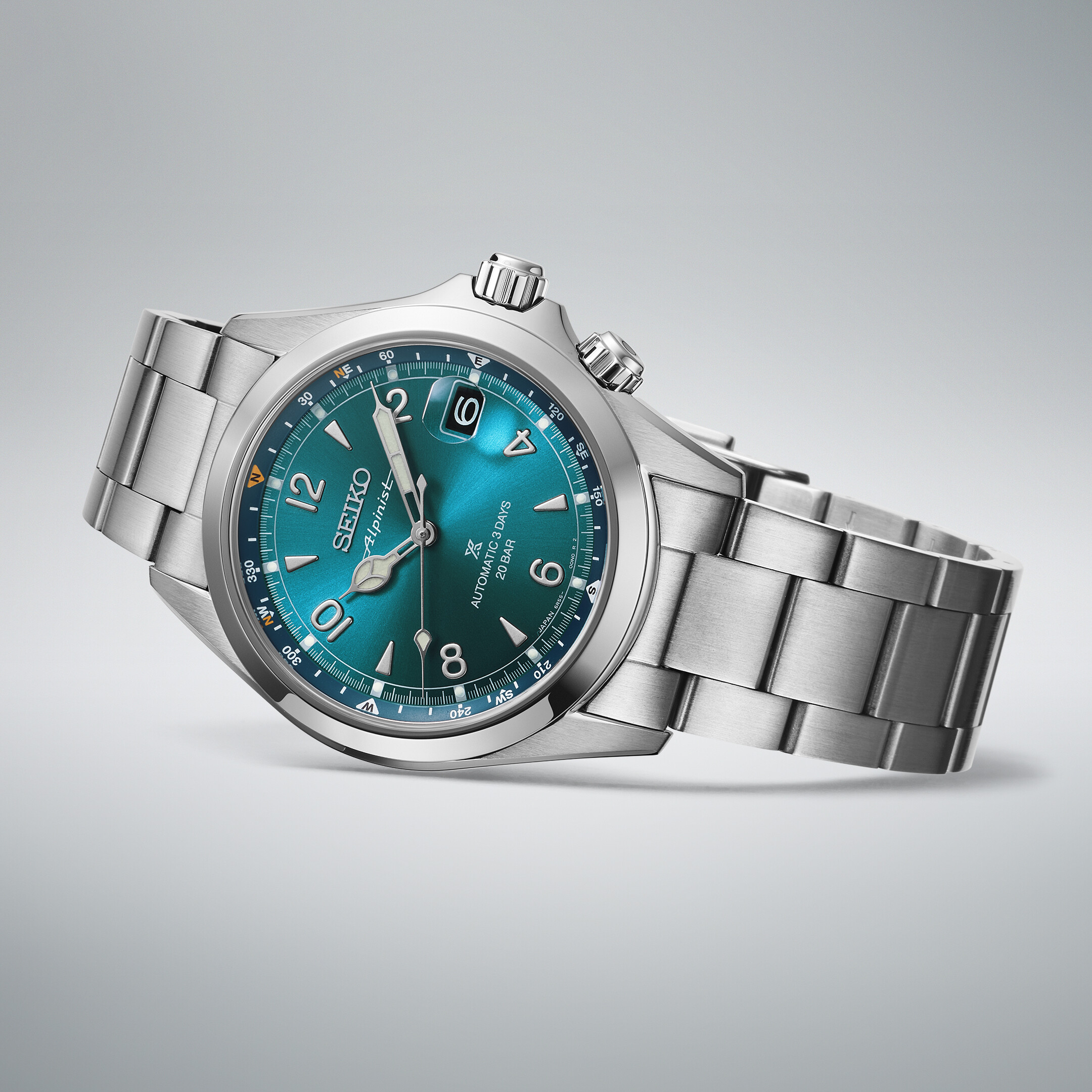 Eine silberfarbene Armbanduhr mit einem türkisfarbenen Zifferblatt mit Kompassmarkierungen und silbernen Zeigern.