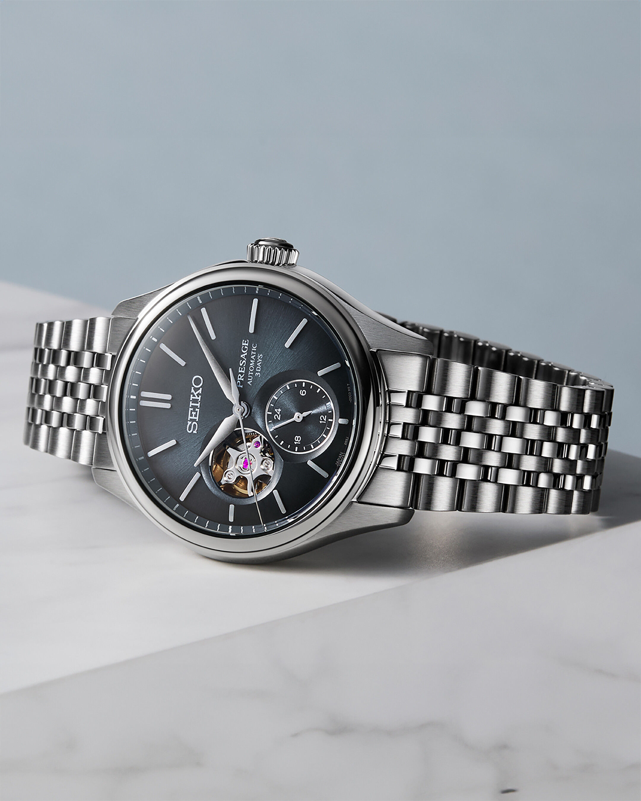 Eine dunkle graue Herrenuhr mit silbernem Armband und einer "Open Heart" Öffnung, die das Uhrwerk zeigt.