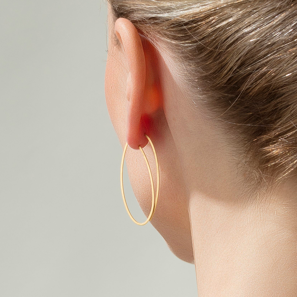 Ein goldenes, oval geformtes Ohrring-Paar mit schlichtem Design hängt am Ohr einer Frau.
