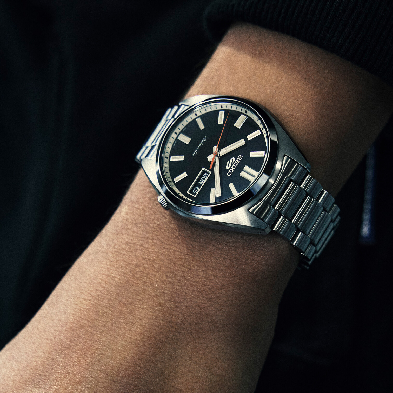 Eine Armbanduhr mit schwarzem Zifferblatt und silbernem Armband, die an einem Arm getragen wird.