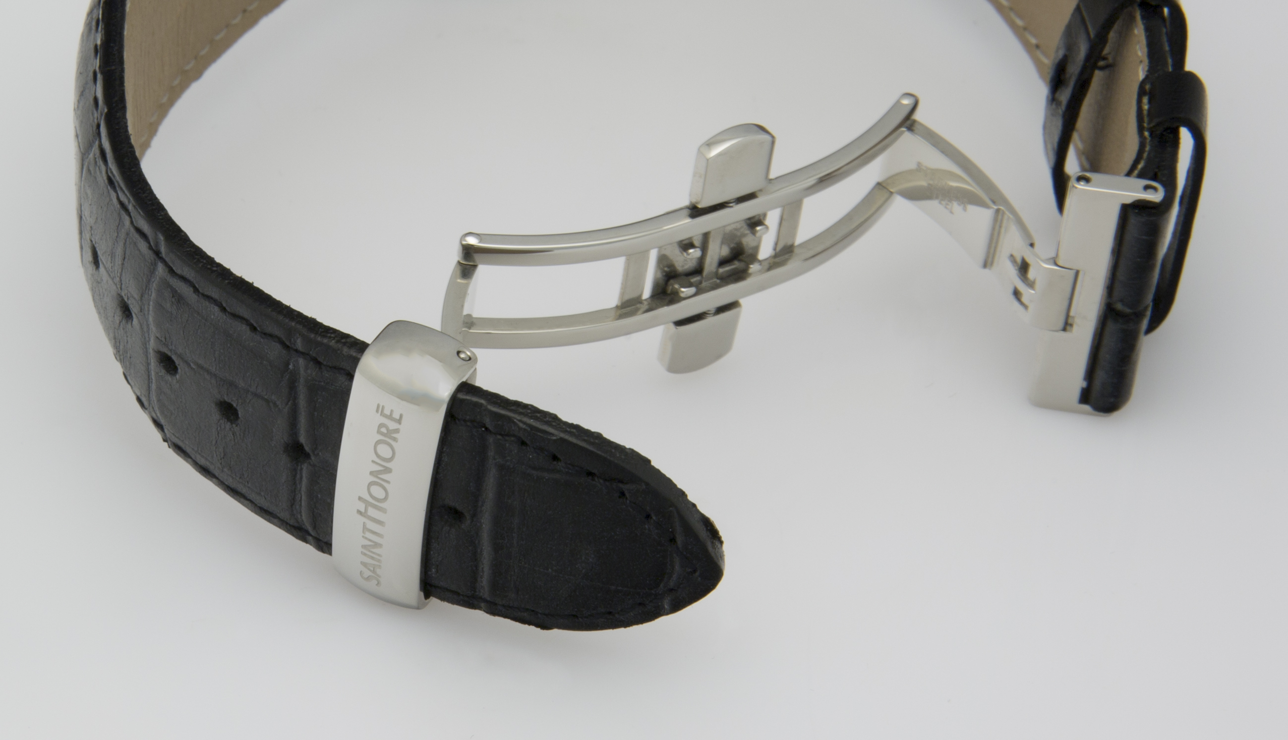 Ein schwarzes, krokodillederartiges Armband mit einer silberfarbenen Faltschließe liegt auf weißem Grund.
