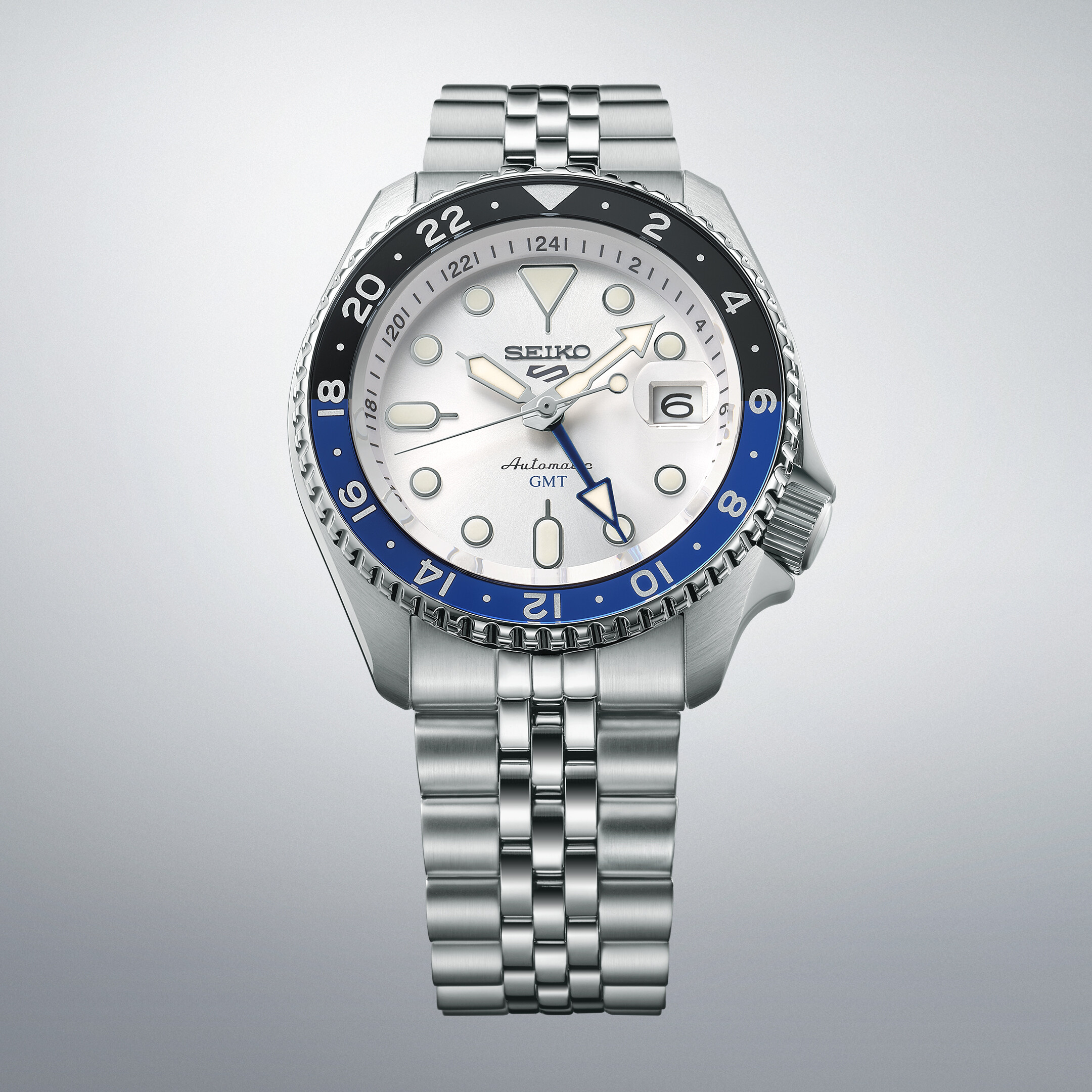 Eine silberne Herrenuhr mit weißem Zifferblatt und blau-schwarzer Lünette mit GMT-Funktion.