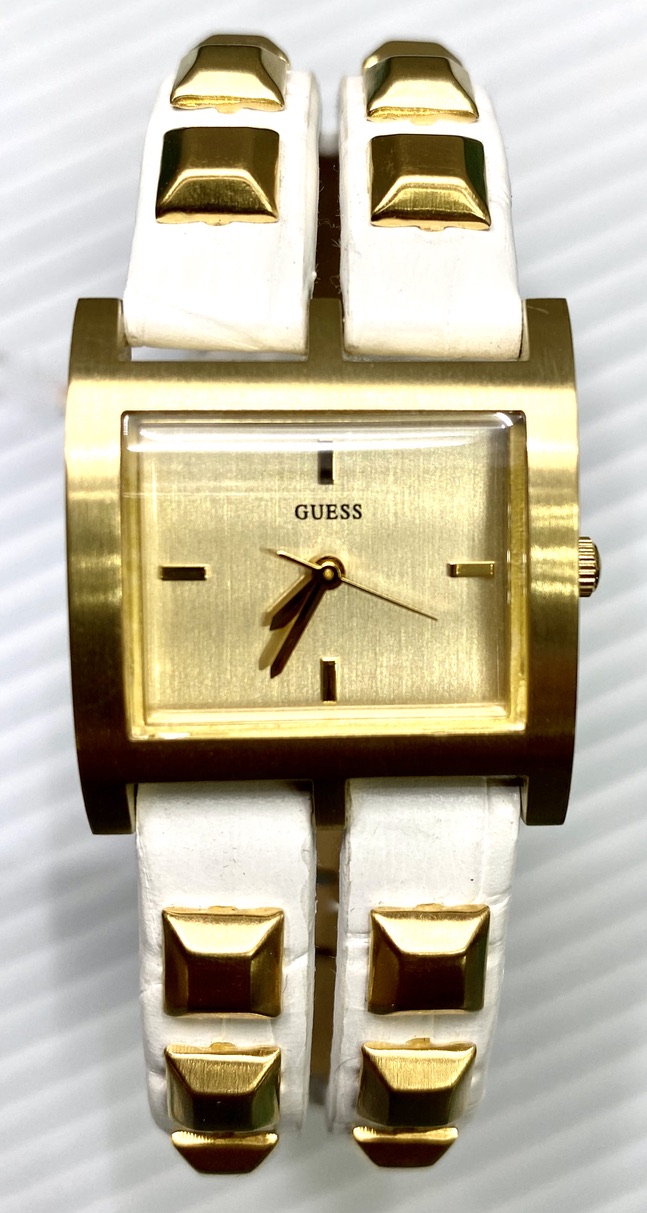 Eine goldene Damenuhr mit einem rechteckigen Zifferblatt und weißem Armband mit goldenen Nieten.