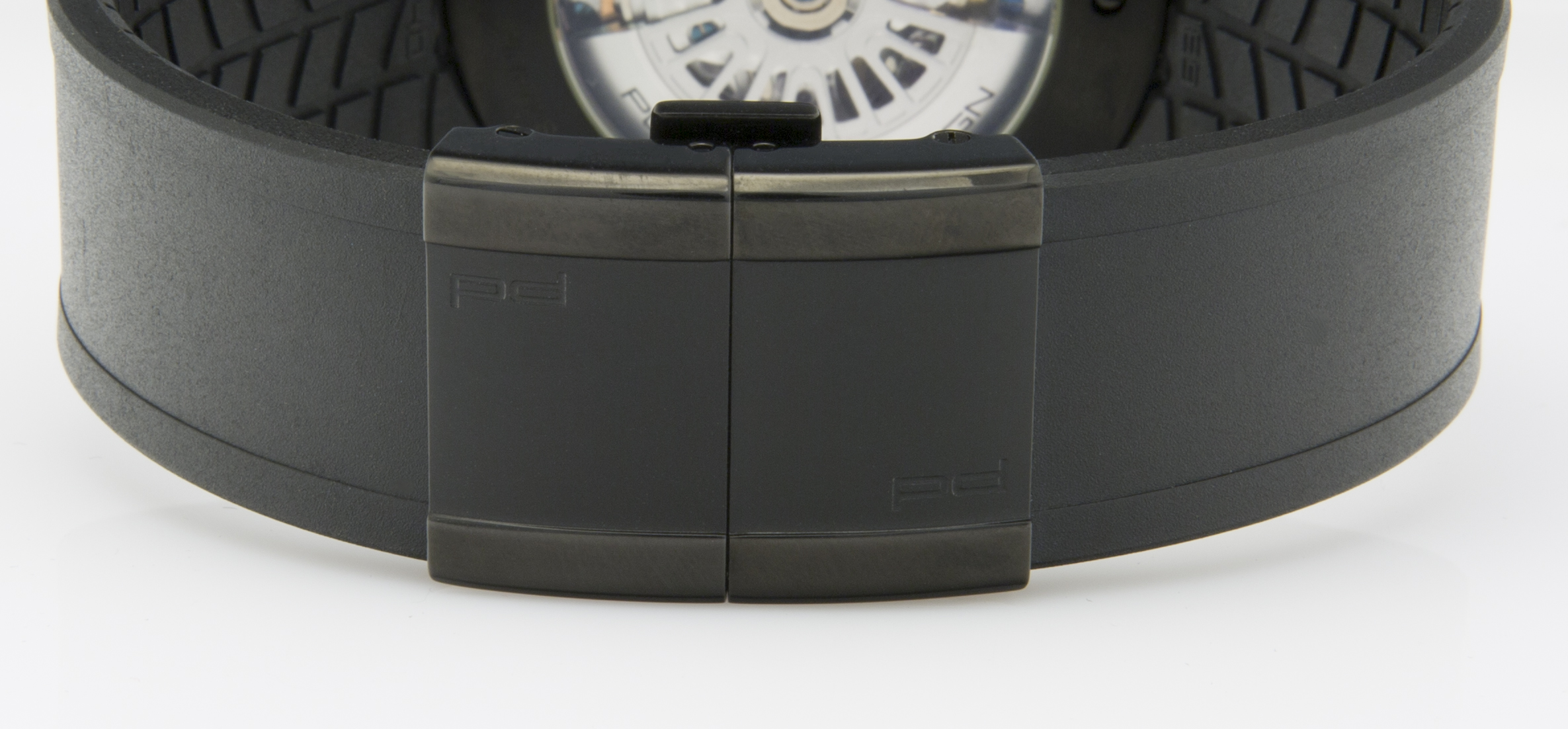 Ein schwarzes Armband mit einer schwarzen Dornschließe zeigt eine detaillierte mechanische Uhr im Hintergrund.