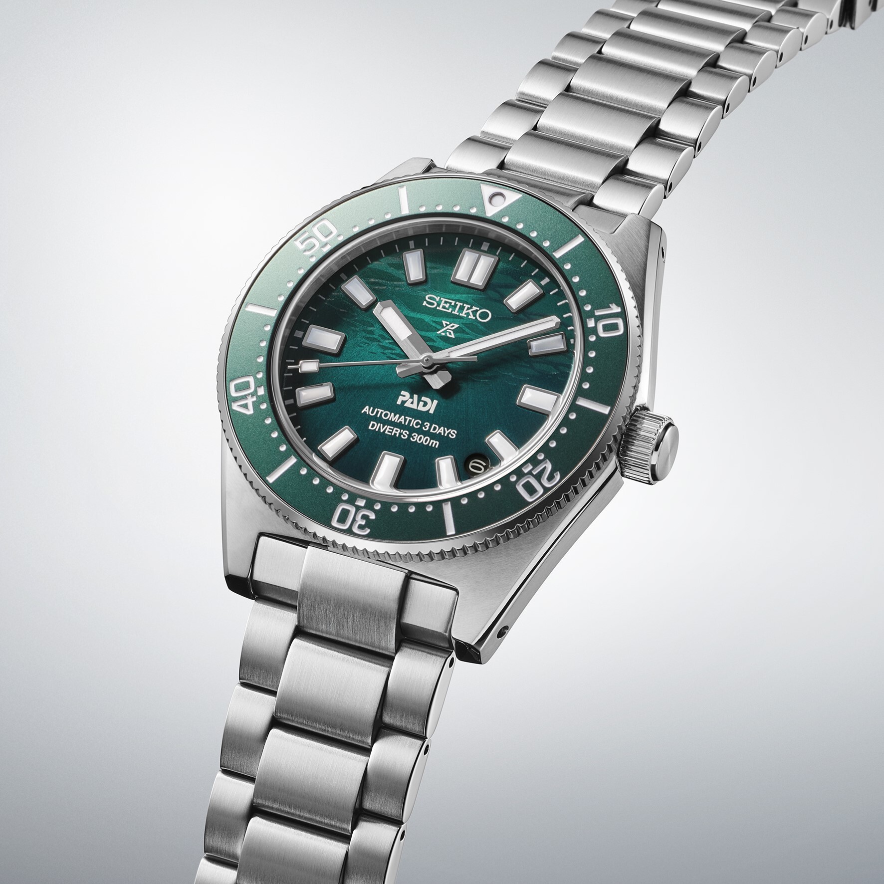 Ein silbernes Armbanduhr mit einem grünen Zifferblatt und einem grünen Drehlünette. Das Zifferblatt hat ein Muster.