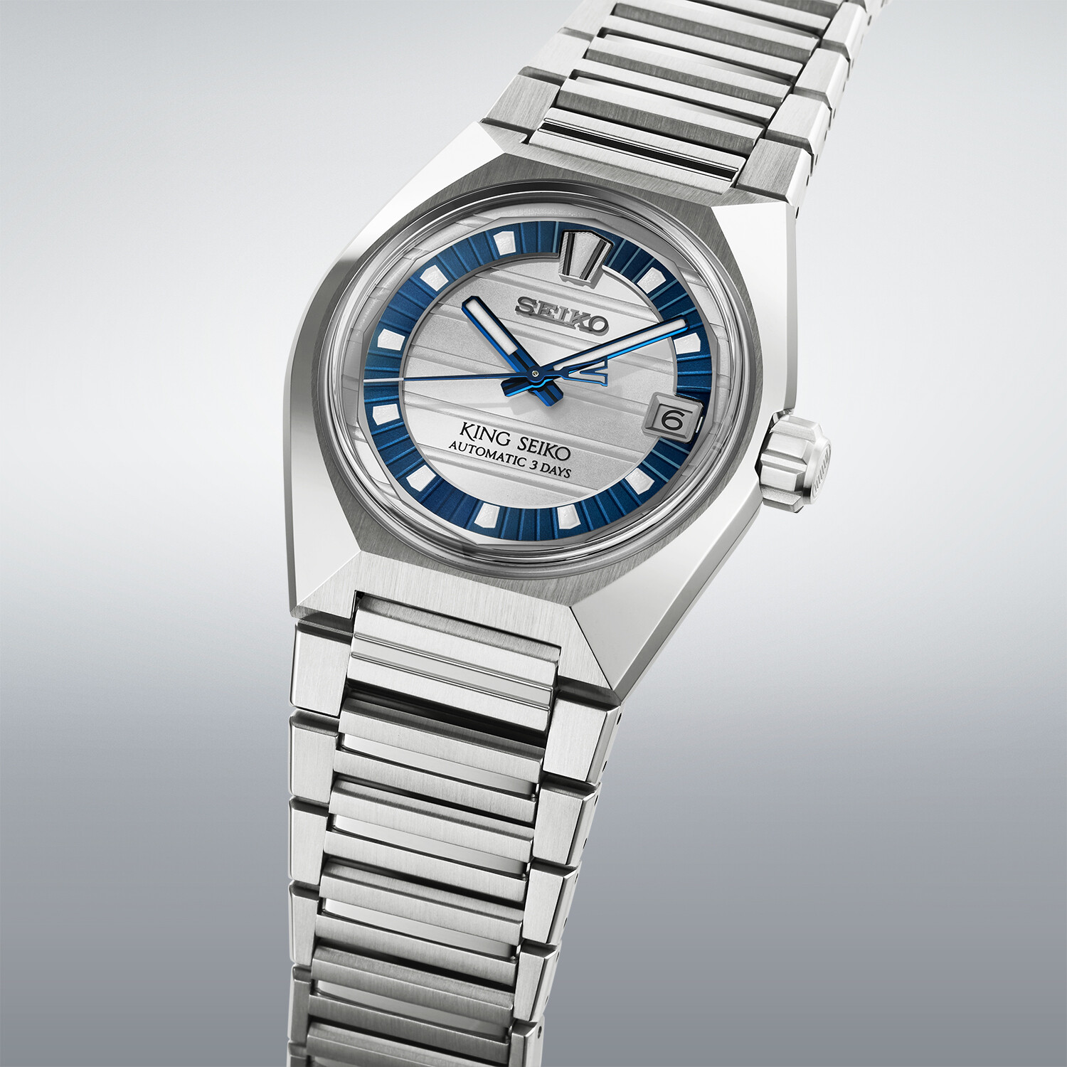 Eine silberne Uhr mit einem blauen Zifferblatt, das ein streifenförmiges Muster aufweist. Das Band ist ebenfalls silberfarben.