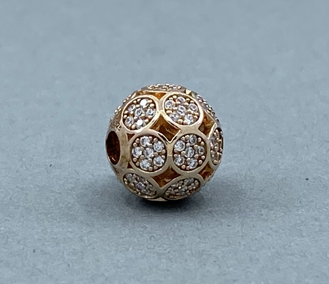 Ein kugelförmiger Anhänger in Gold mit kleinen, funkelnden Steinen in kreisförmiger Anordnung