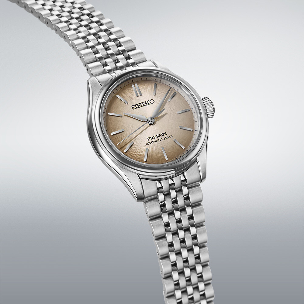 Eine silberne Uhr mit einem champagnerfarbenen Zifferblatt, das feine Linien aufweist. Die Uhr hat ein silbernes Gliederarmband.