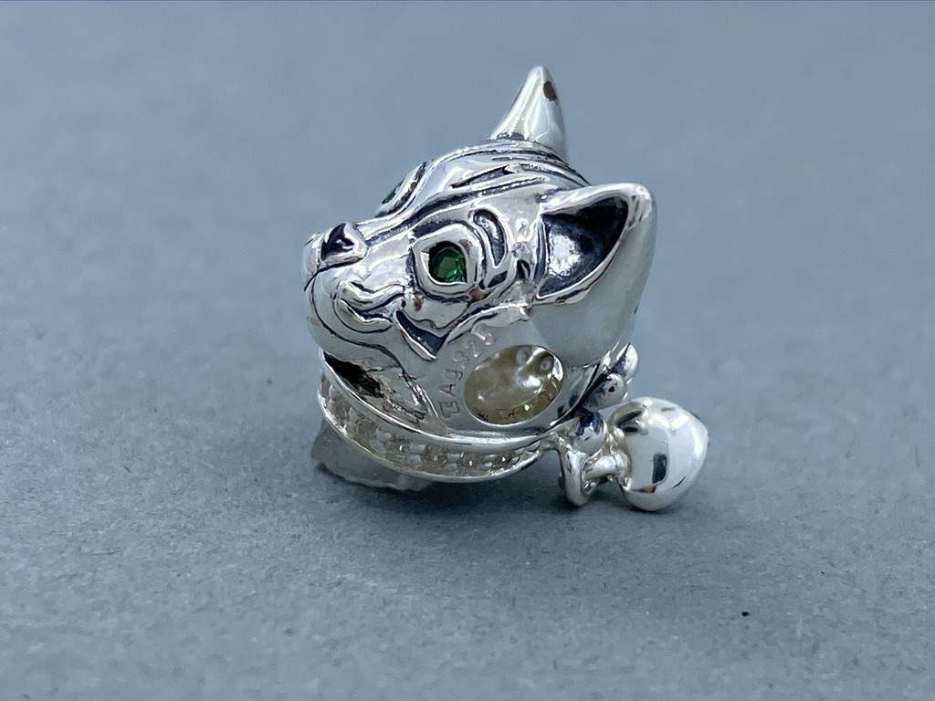 Eine silberne Katzenfigur mit grünen Augen und einem kleinen Ball am Halsband.